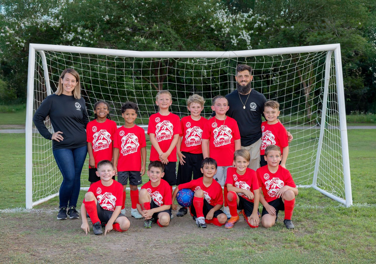 Youth soccer team in red jerseys posing in front of a goal net on a grass field.