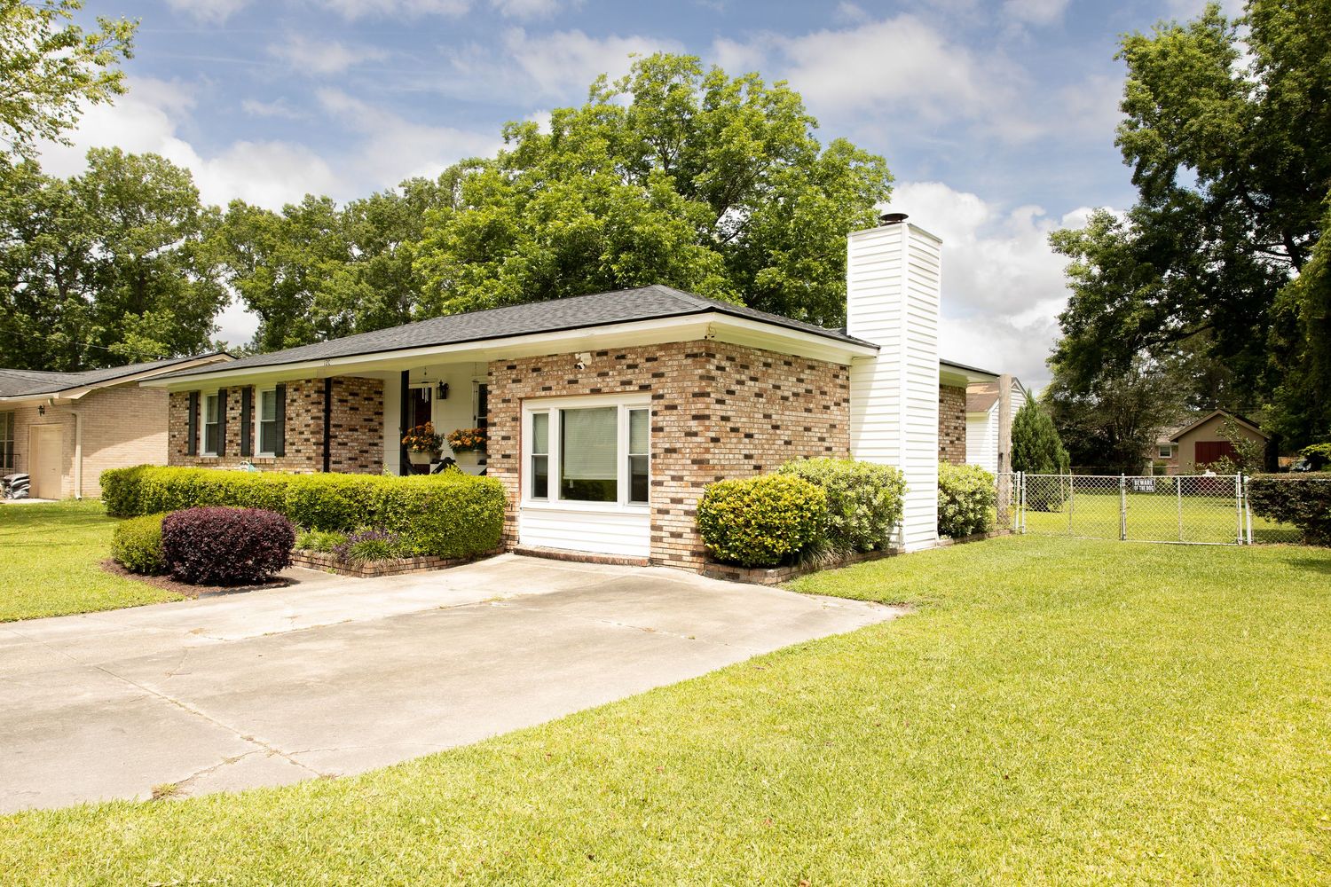 Panoramic view of a suburban house with brick exterior and well-maintained lawn on a sunny day.