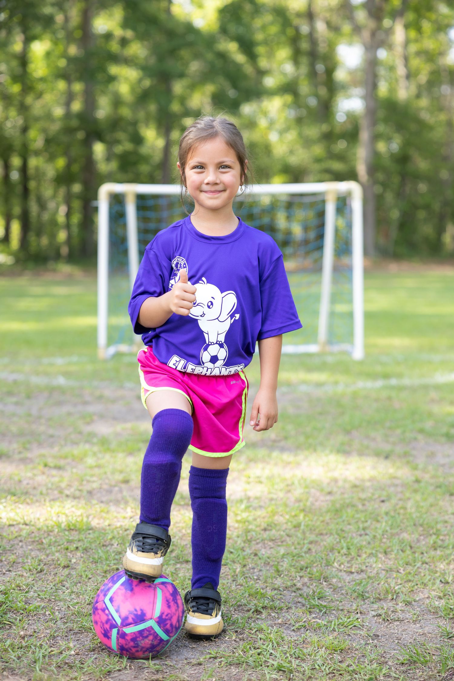 Soccer player in purple shirt posing with pink and white ball on field.