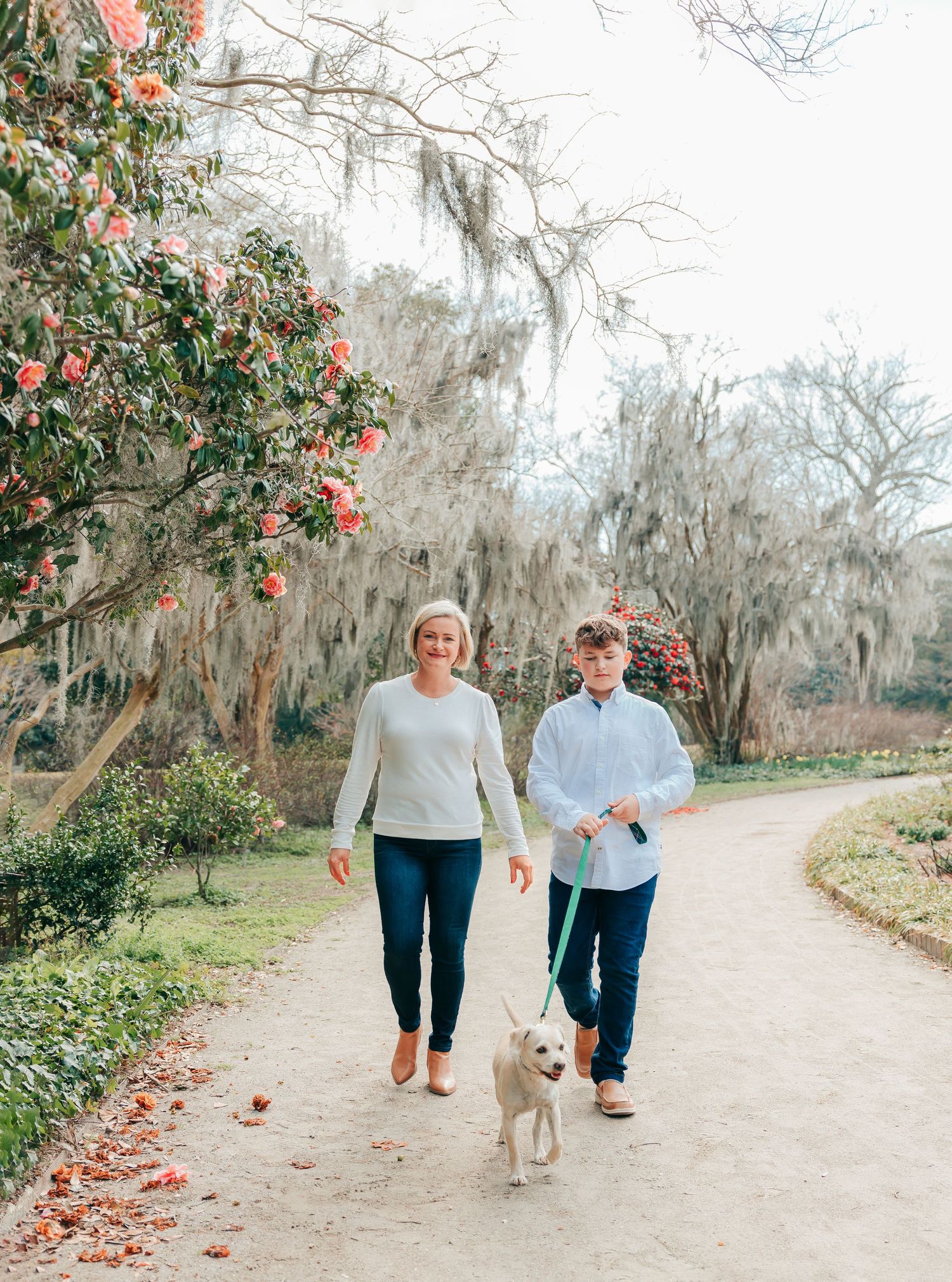 Couple walking hand in hand down a scenic path lined with Spanish moss and camellia bushes.