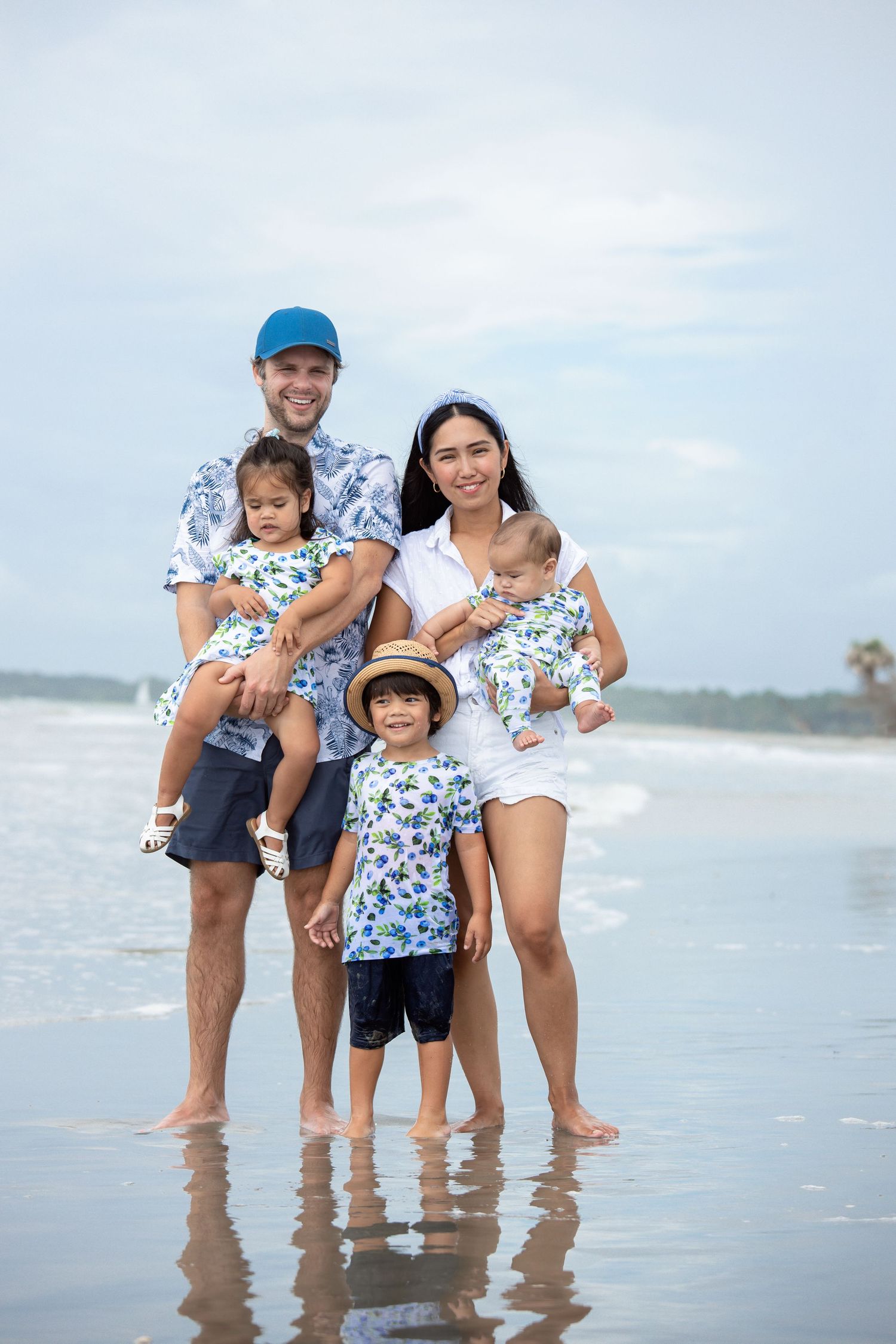 Family members in matching floral prints play together at the ocean's edge.