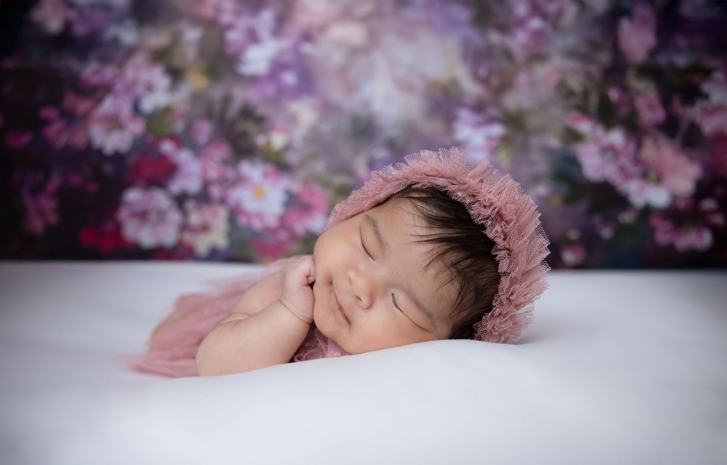 Artistic newborn photography with pink cherry blossoms and purple tones.