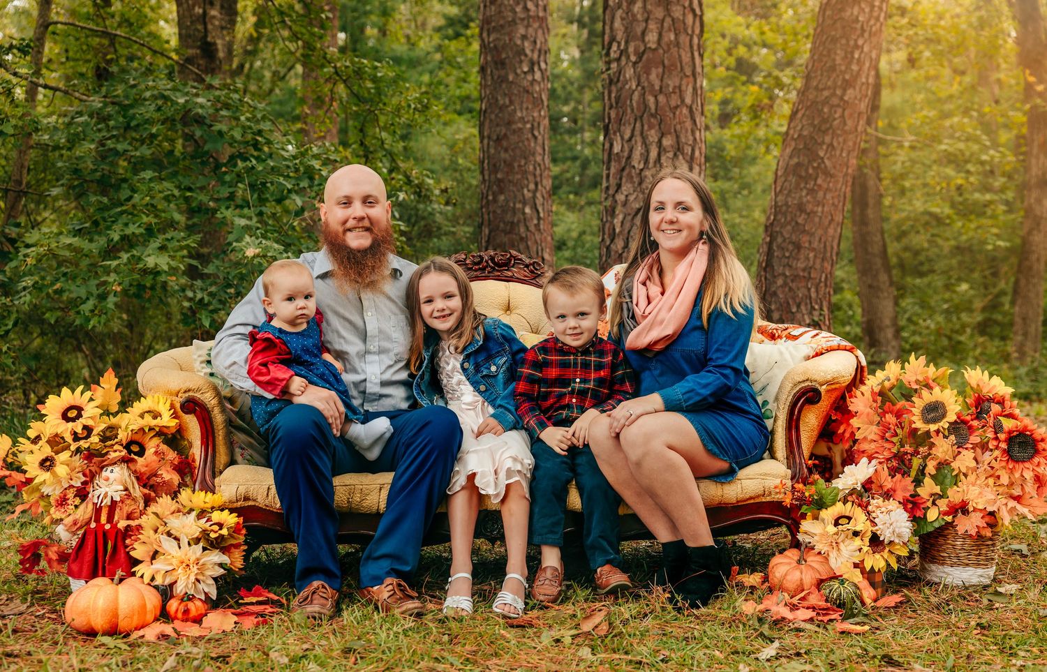 Fall family photo session in a forest with pumpkins and autumn leaves at sunset.
