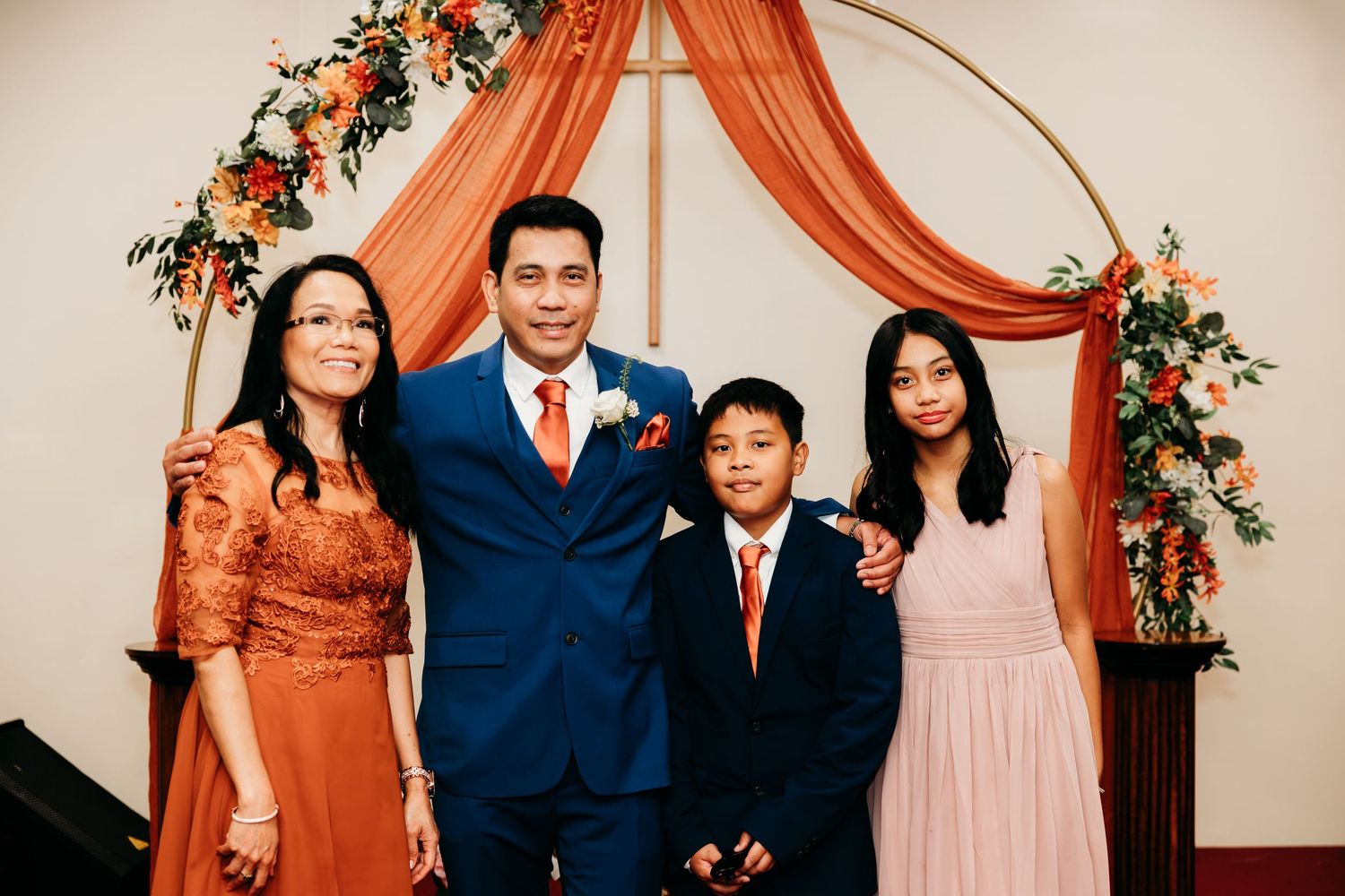 Wedding ceremony setup with burnt orange draping and floral arch decorations.