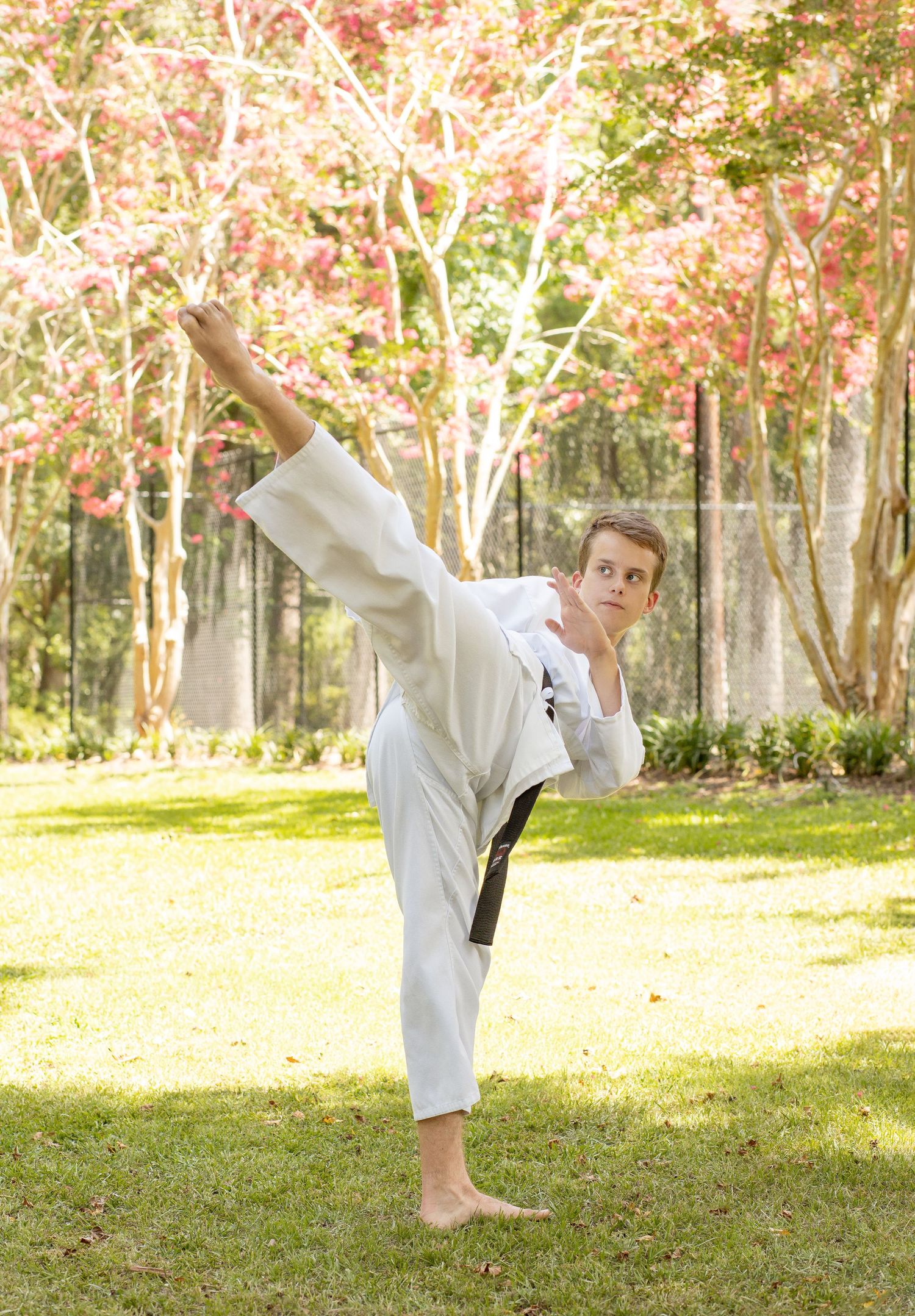 Martial artist demonstrates high kick moves in white uniform against autumn trees.
