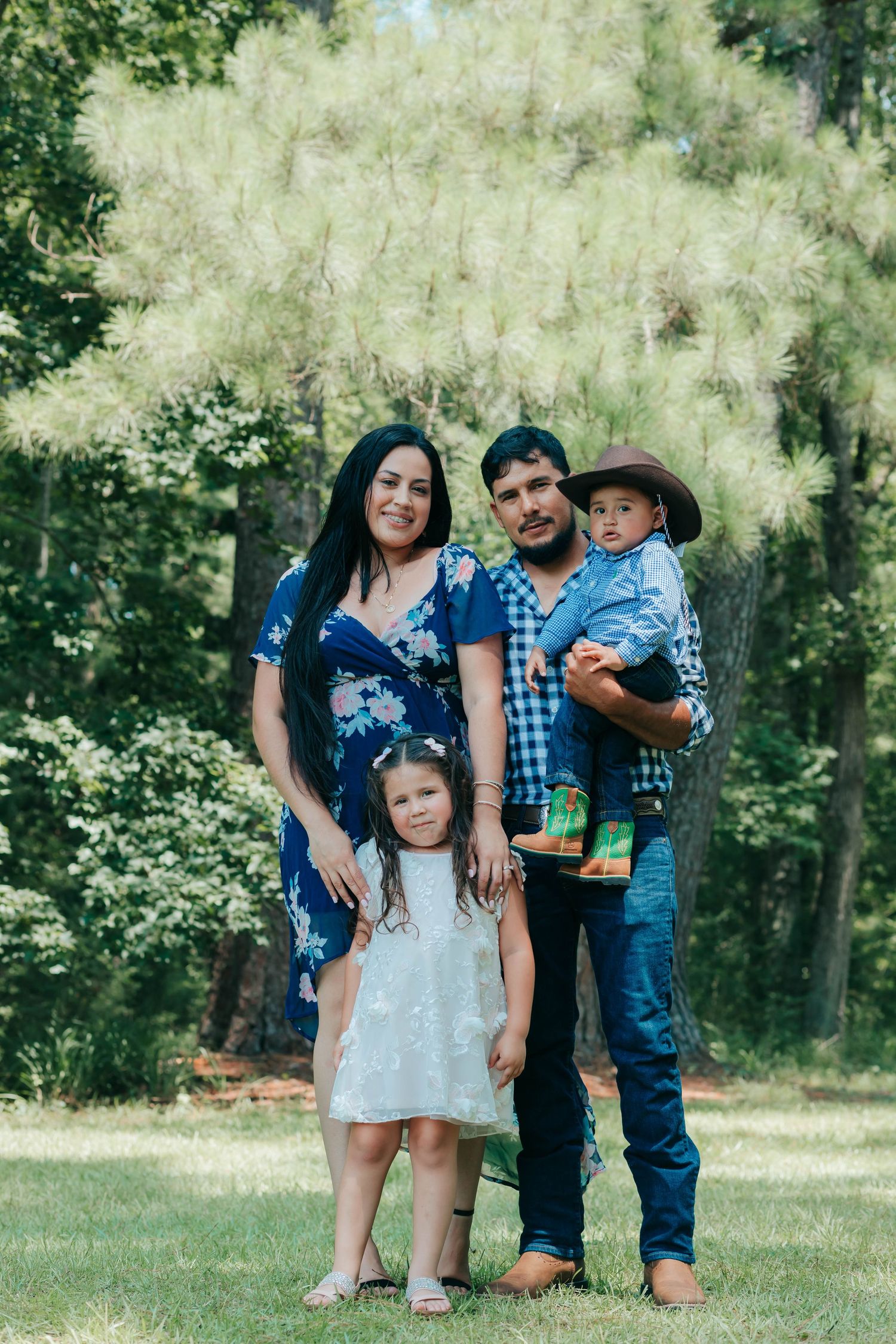 Family group poses together on grassy lawn during outdoor summer photo session.