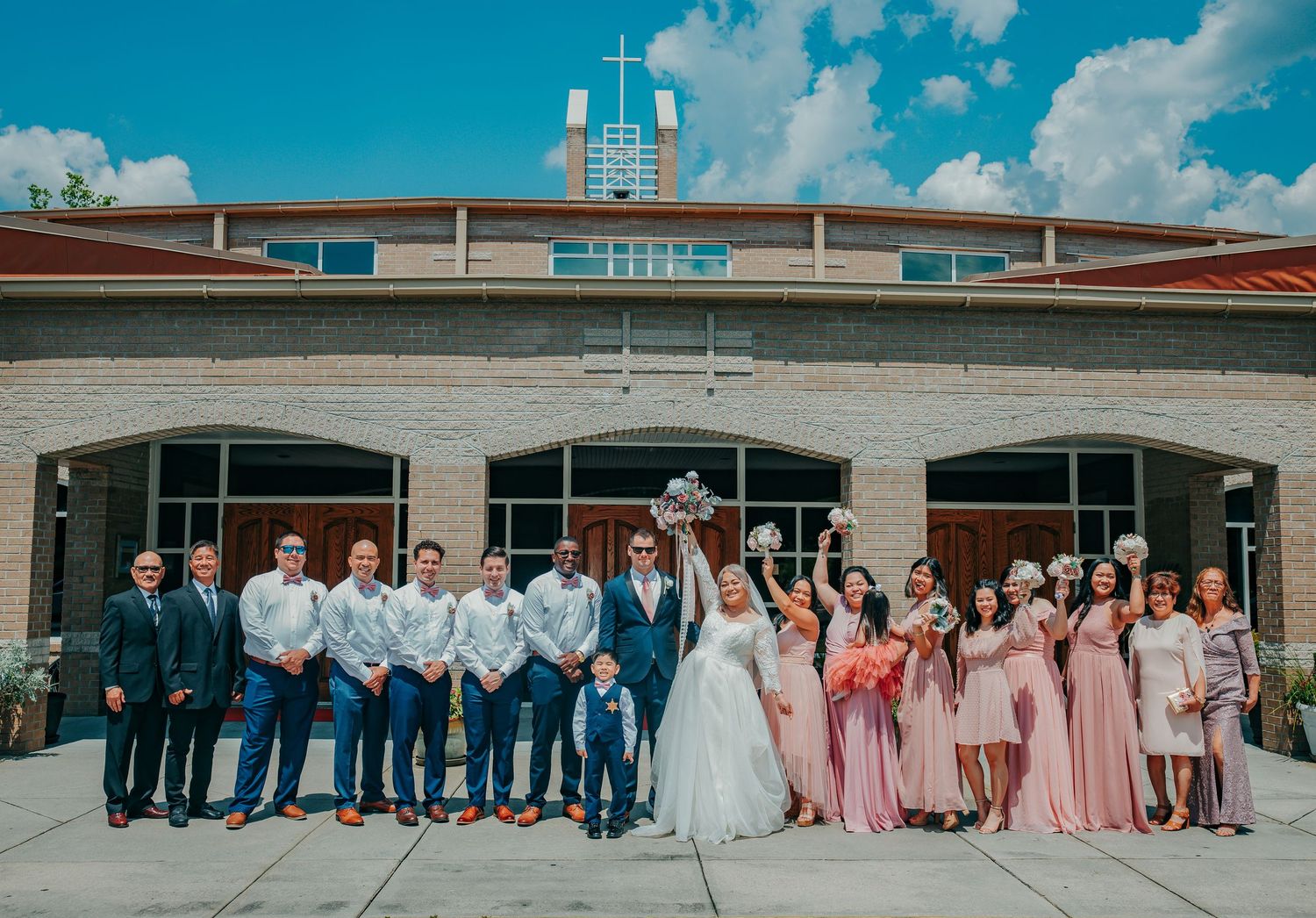 Panoramic outdoor shot of wedding party lined up in front of modern church building.