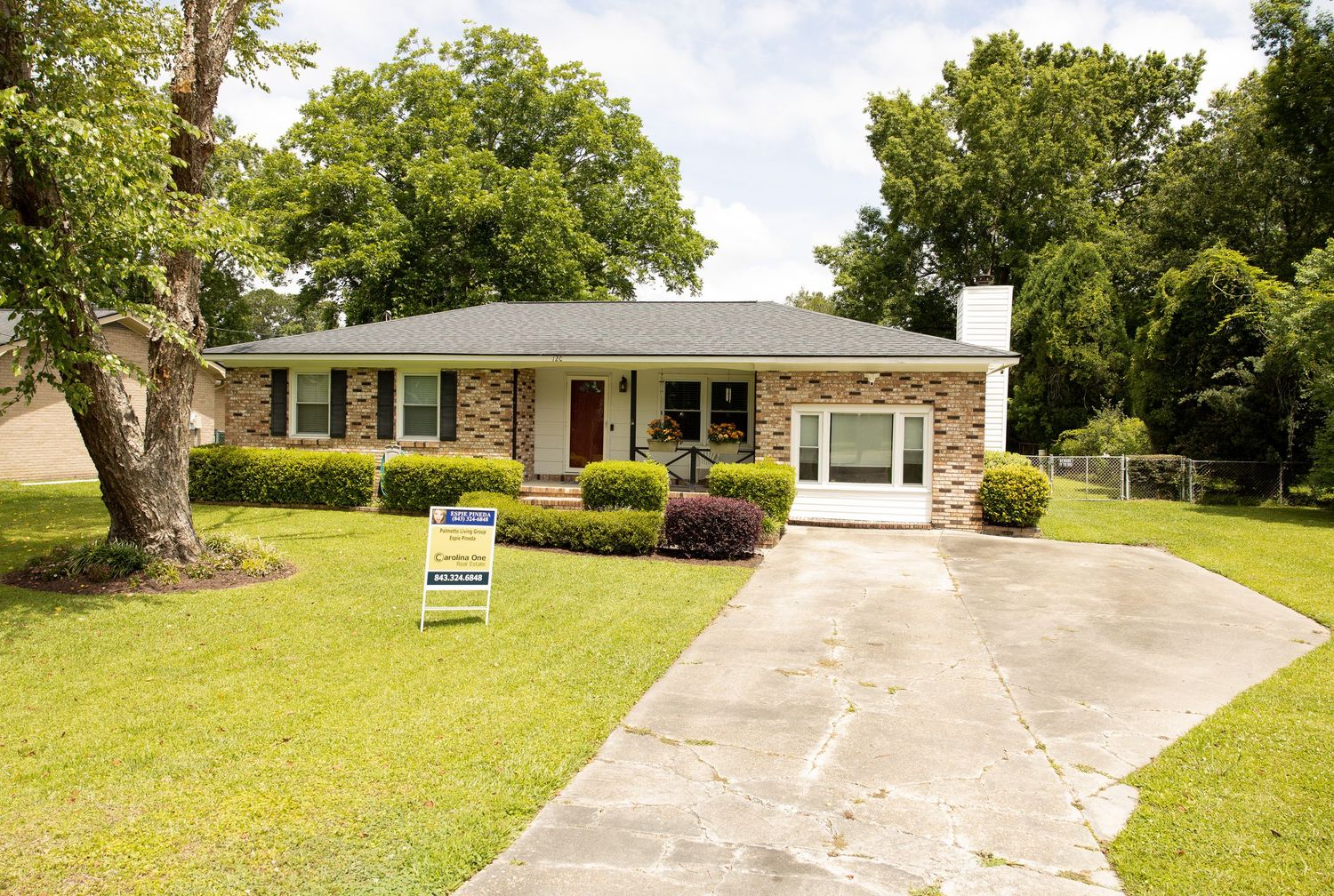 Exterior view of a single-story brick house with attached garage and mature trees.