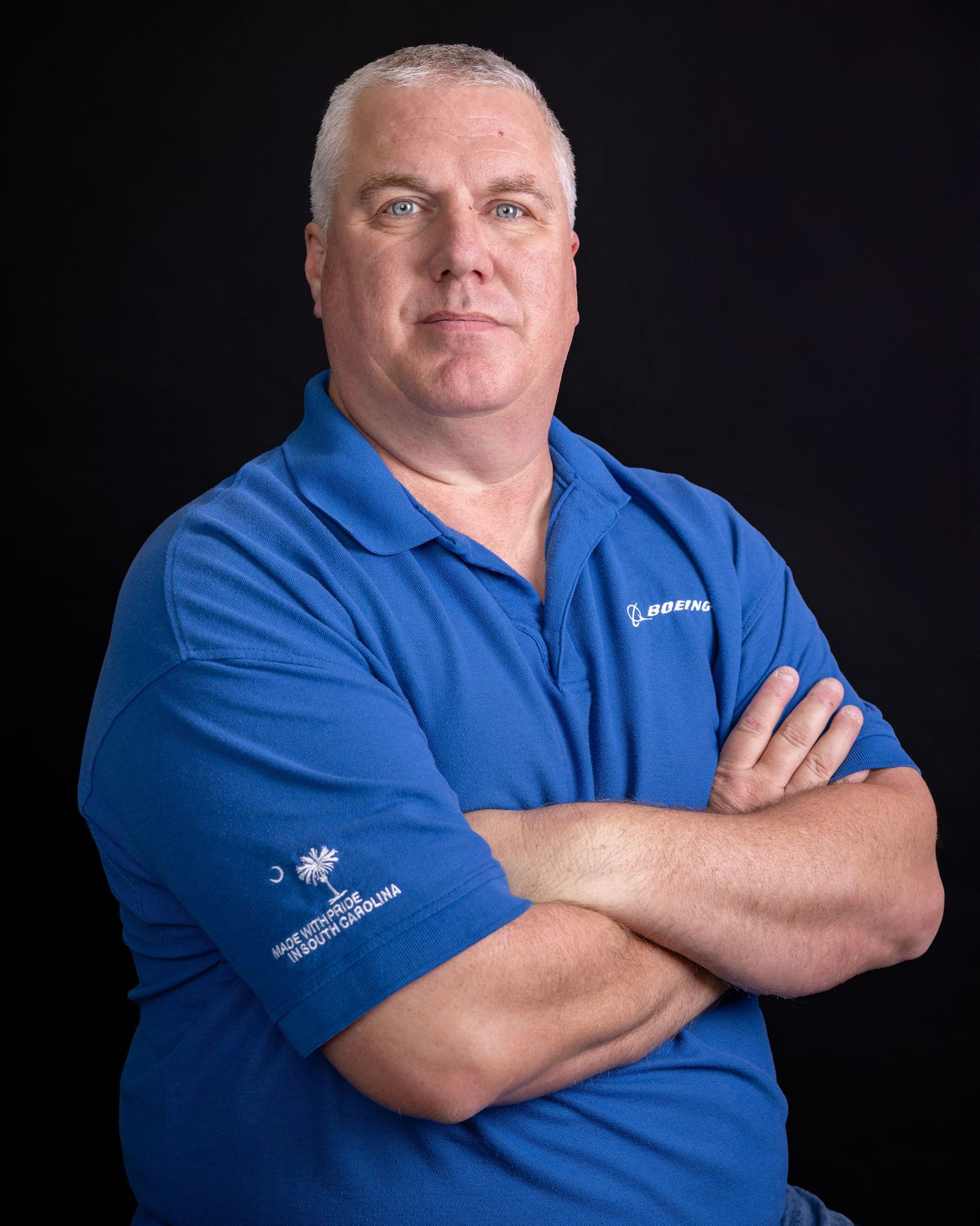 Corporate portrait of person in Boeing uniform with arms crossed against black backdrop.