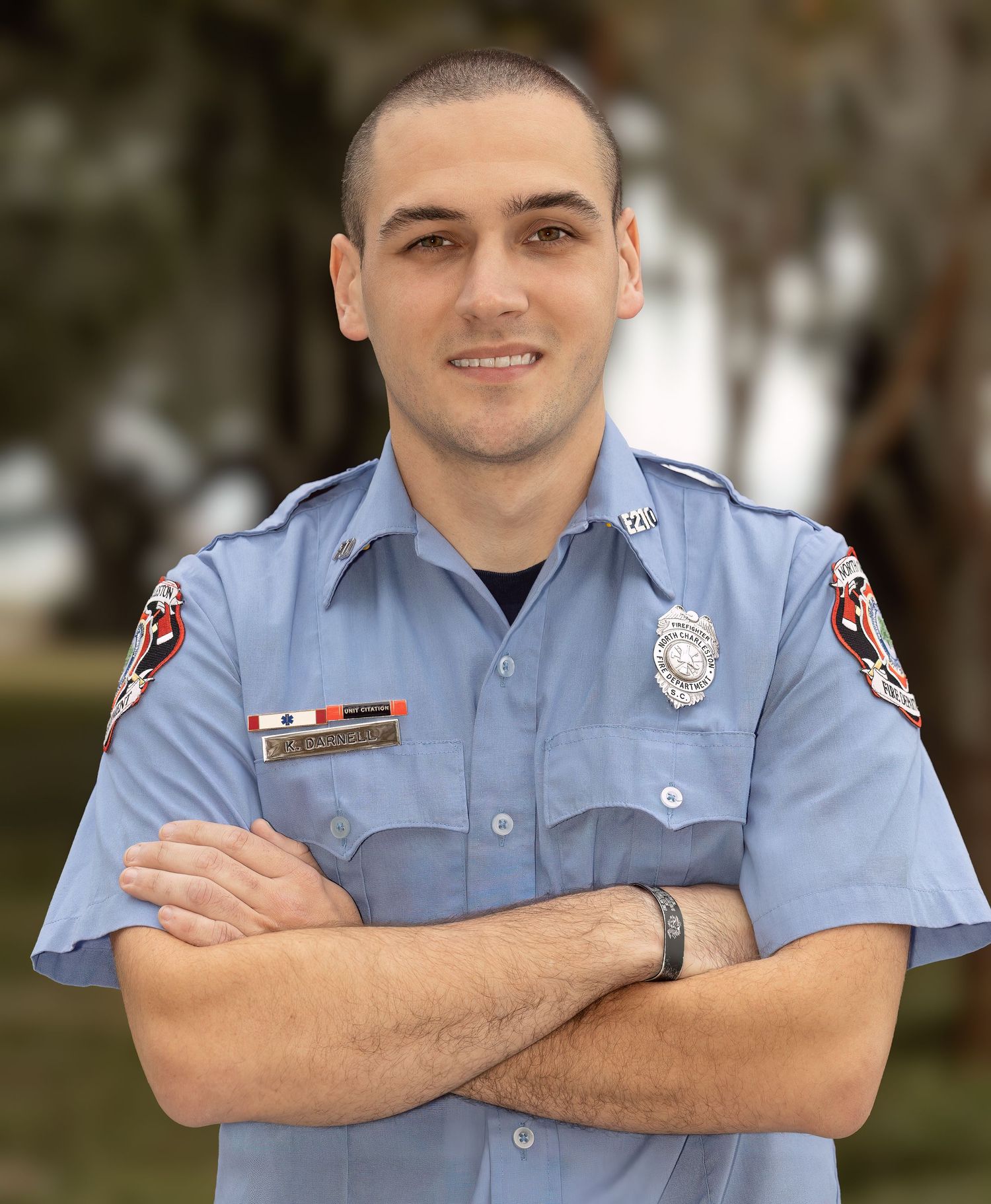 Firefighter in light blue uniform posing against natural background.
