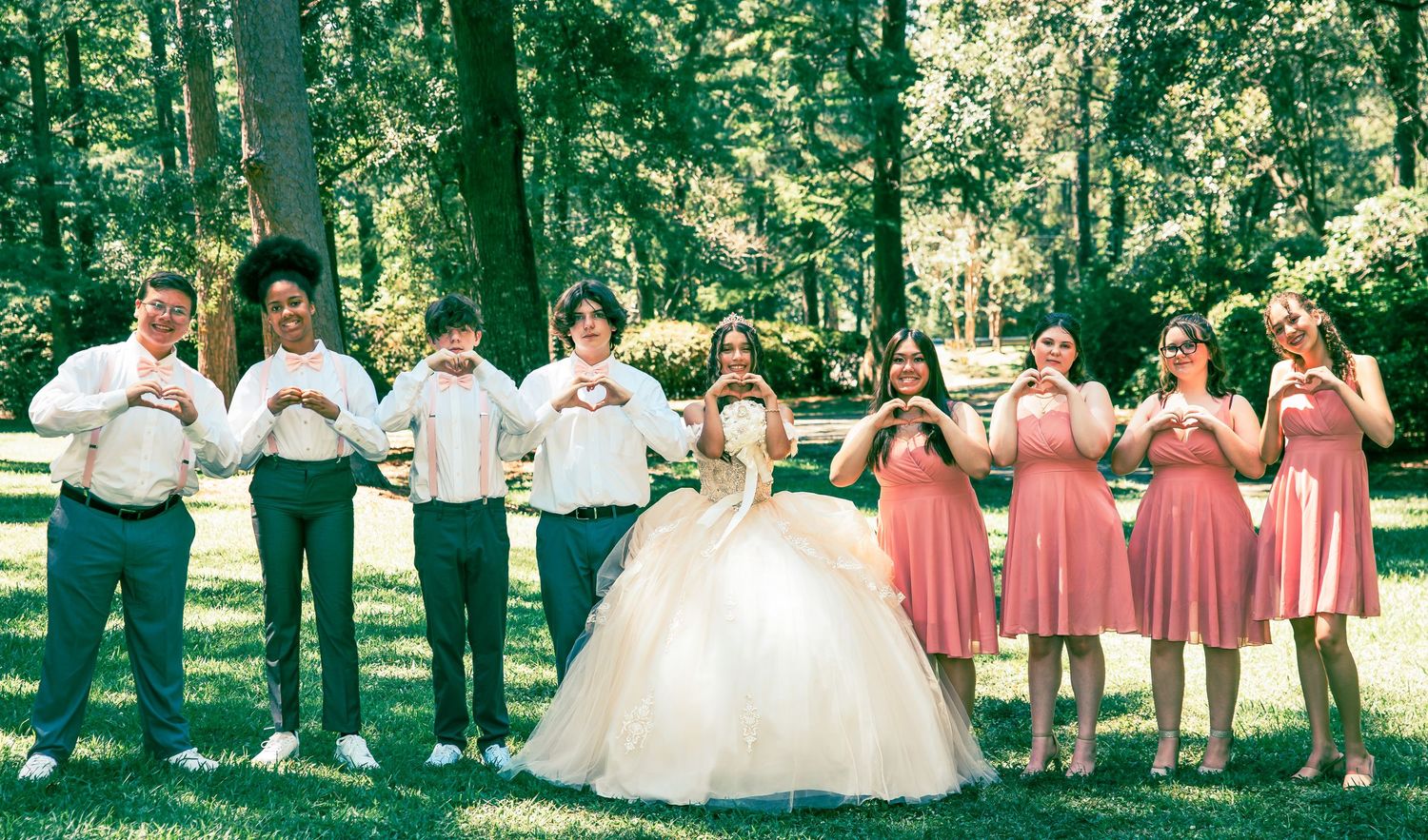 Wedding party in coral dresses and formal attire poses together outdoors in a garden setting.