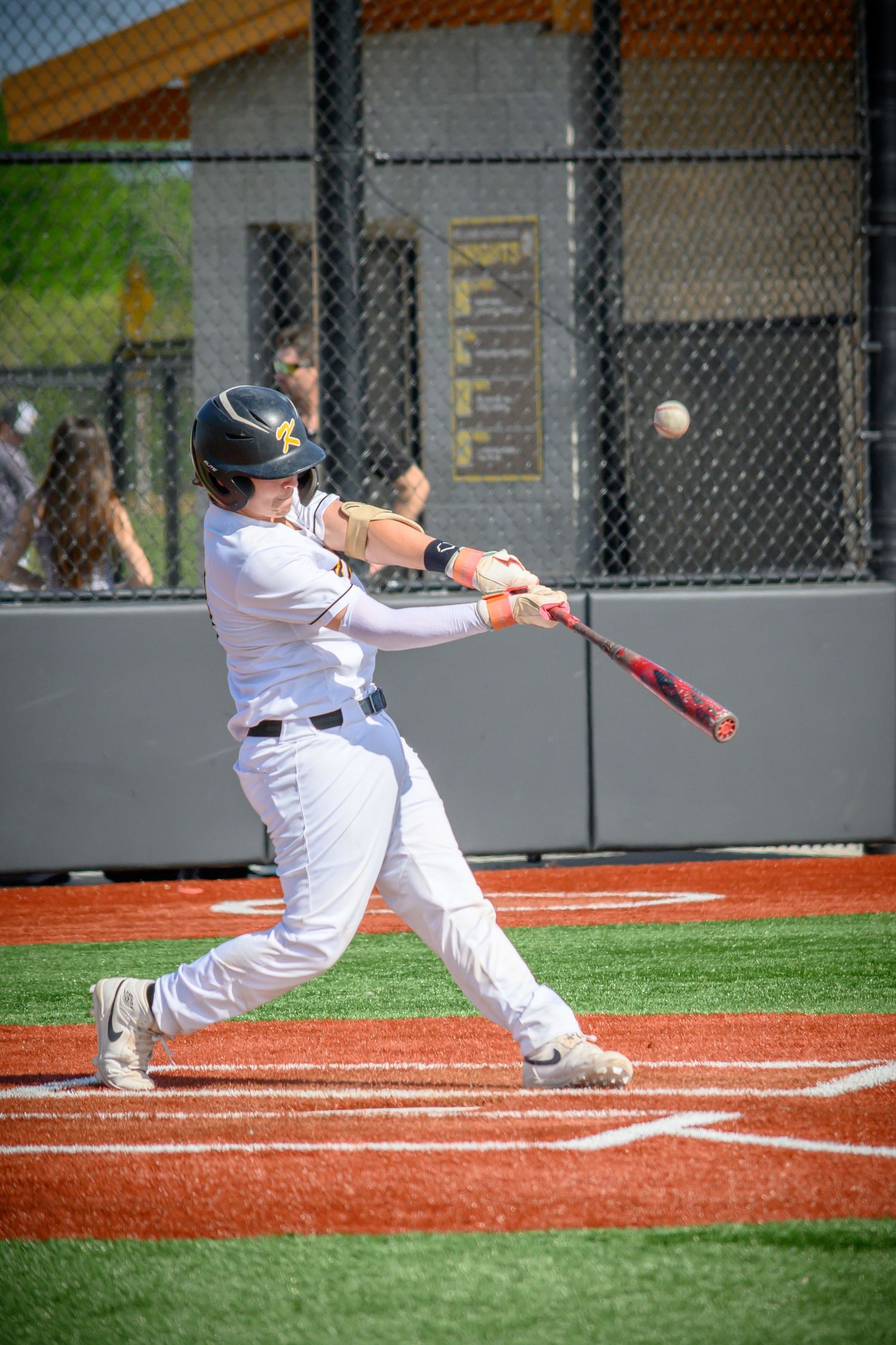 Baseball player in white uniform swings bat to hit ball during game on red clay field.