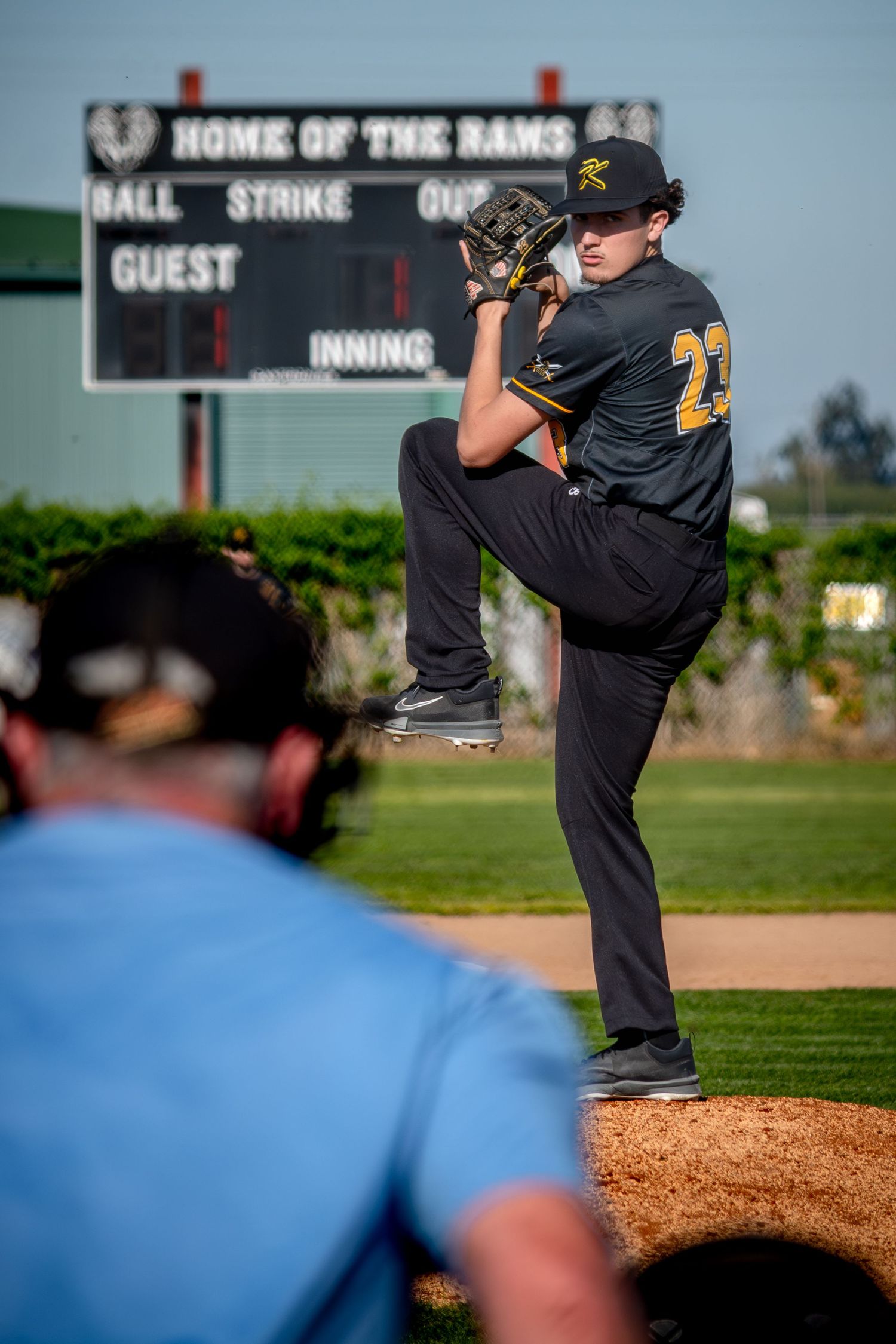 Baseball pitcher on mound in black uniform winds up for pitch during game at home field ballpark.