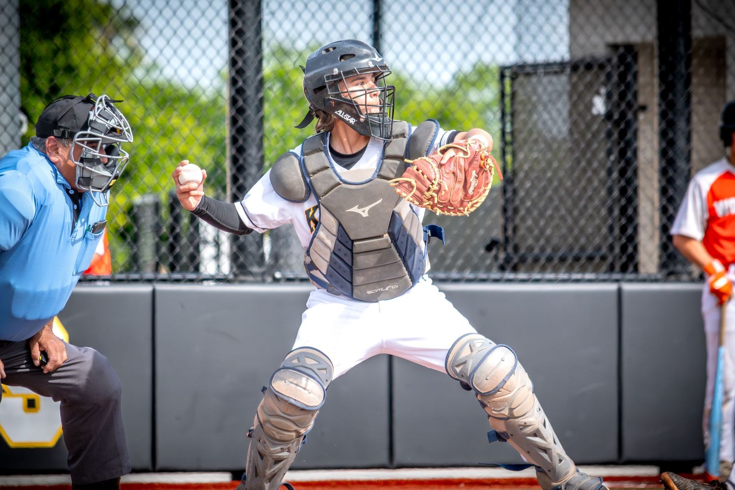 Baseball catcher in full gear crouching in ready position on field during a game.