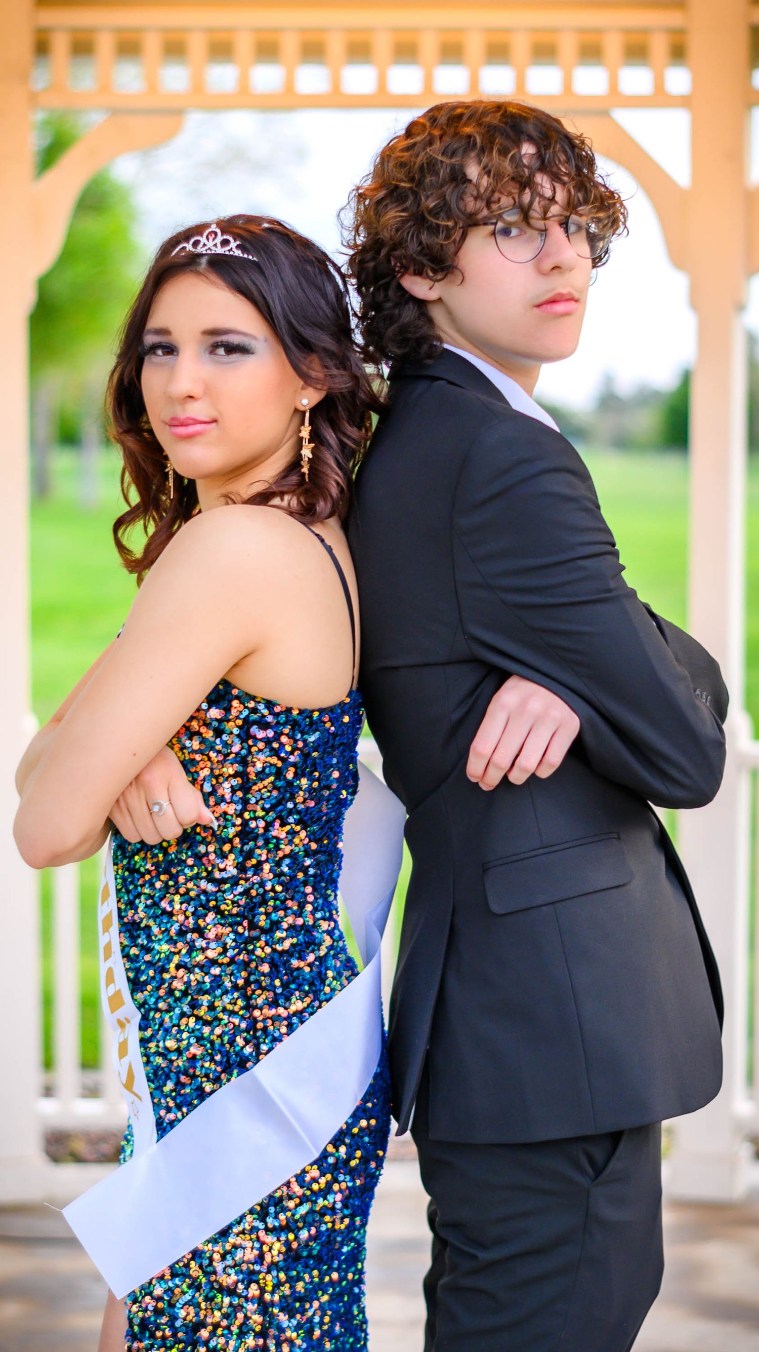 Formal couple poses together in gazebo, wearing sparkly dress and black suit.