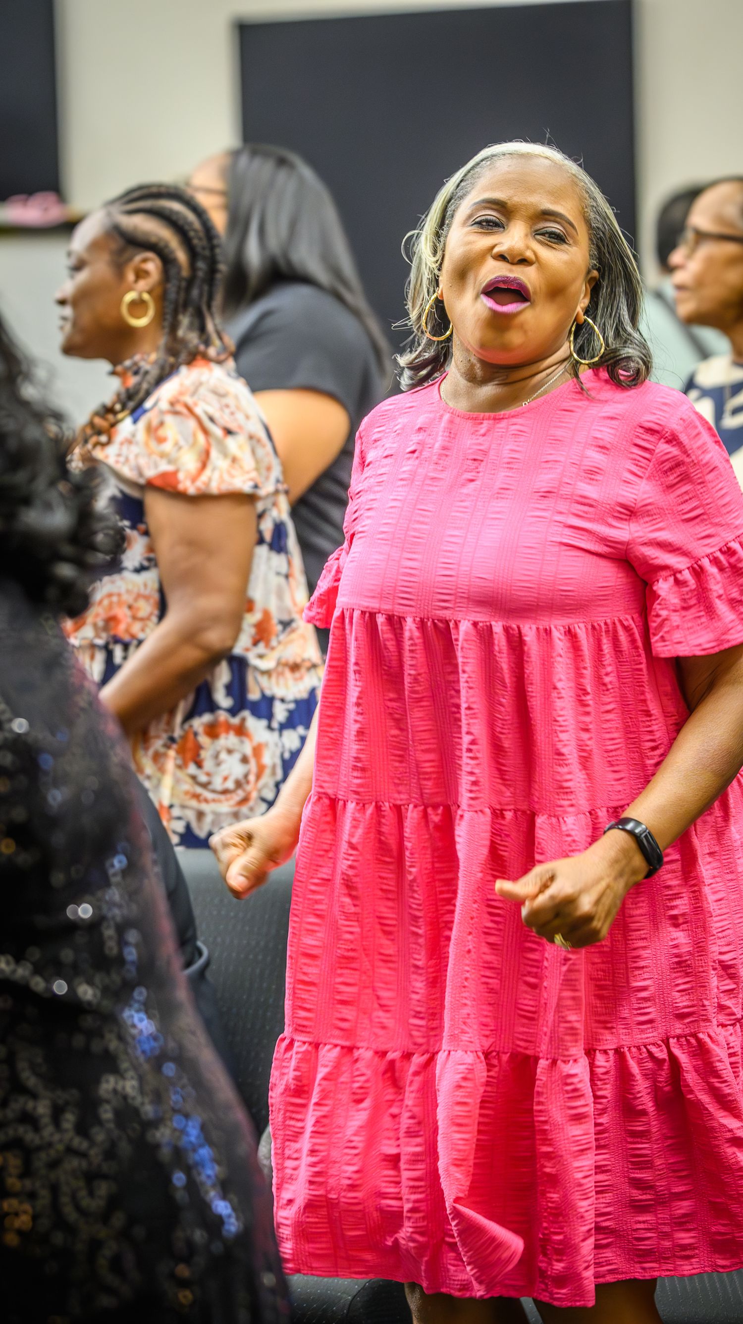 A person in a bright pink ruffled dress dances joyfully during a celebration.