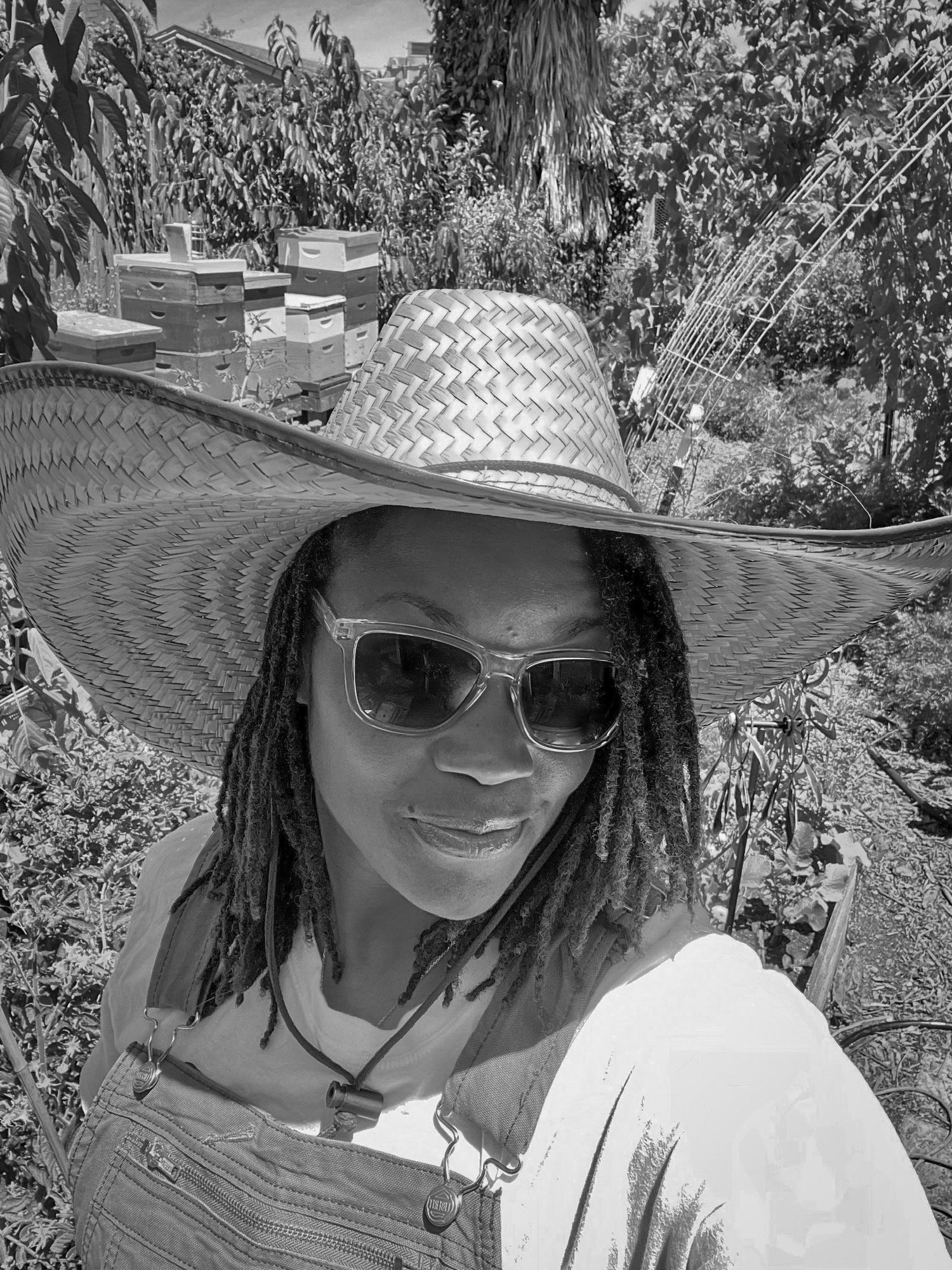 Black and white portrait with sunglasses and straw hat in natural setting.