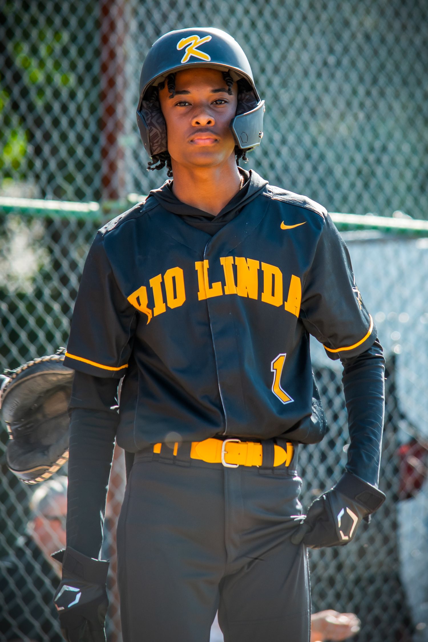 Baseball player in dark uniform with yellow lettering runs during game.
