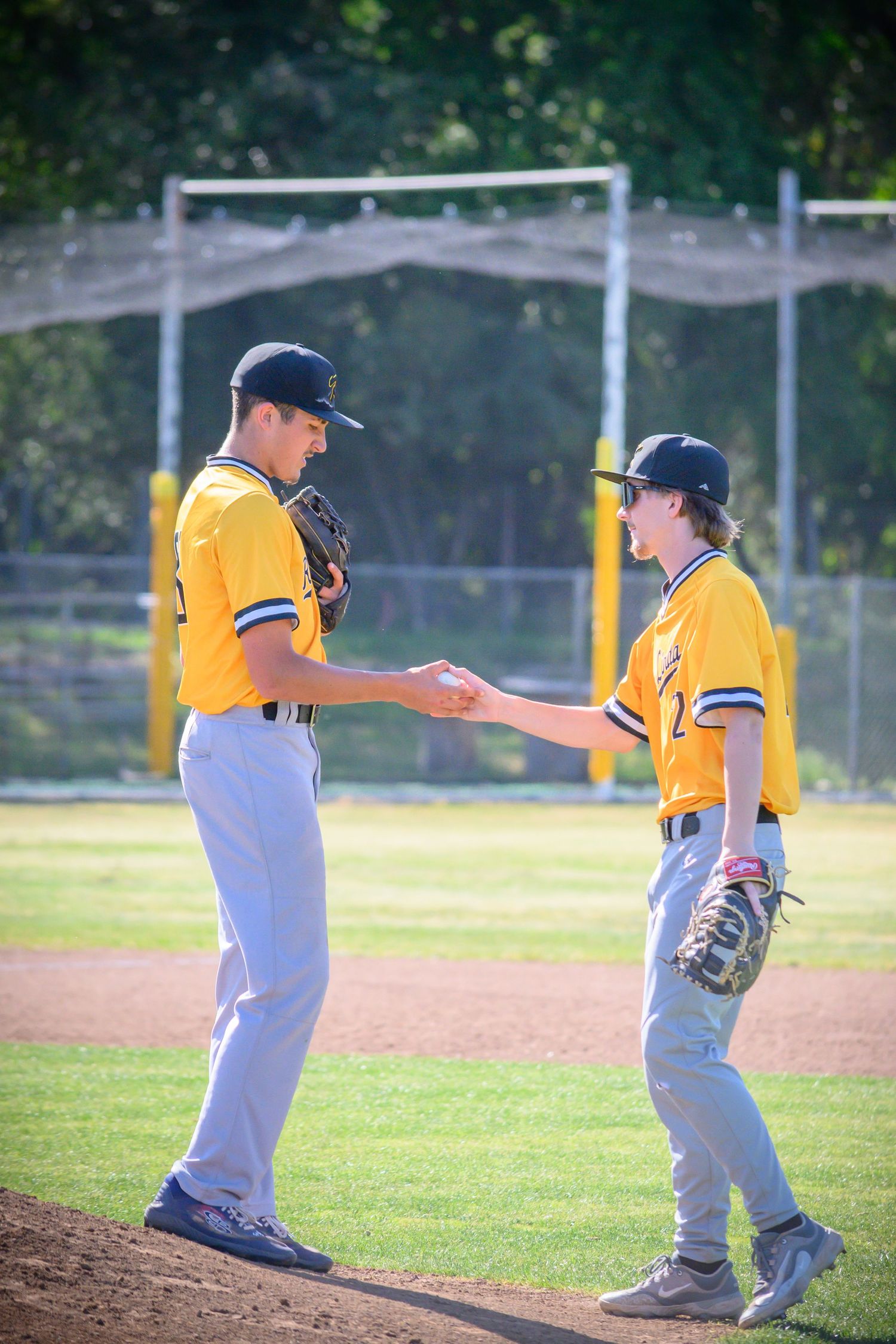 Two baseball players in yellow uniforms interact on pitcher's mound during game.