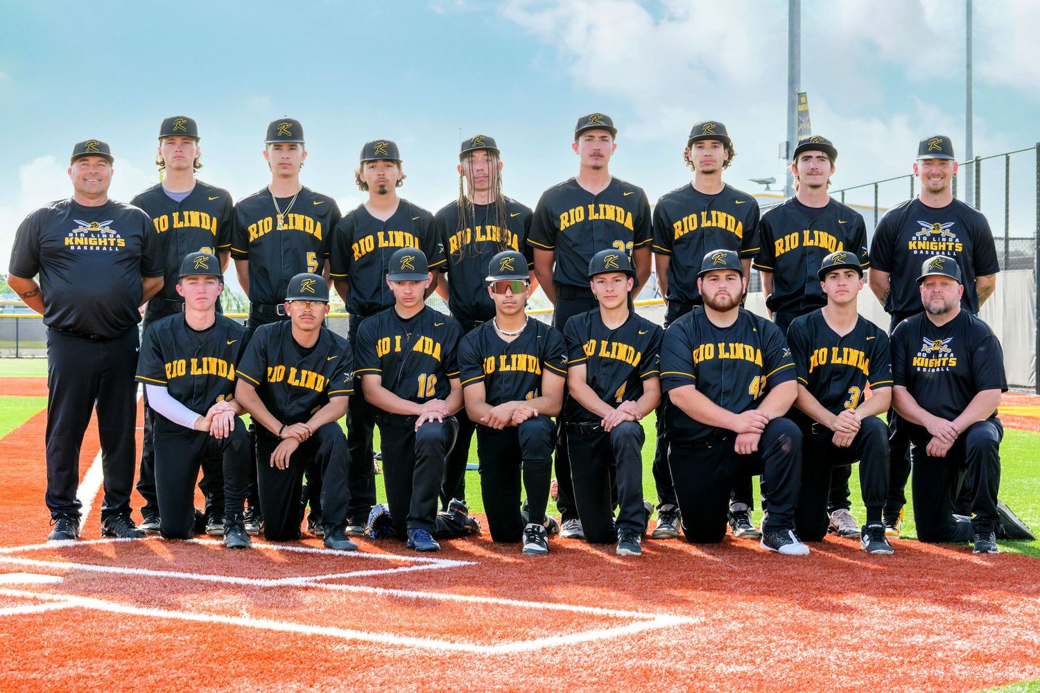High school baseball team members pose together in black uniforms on a track field.