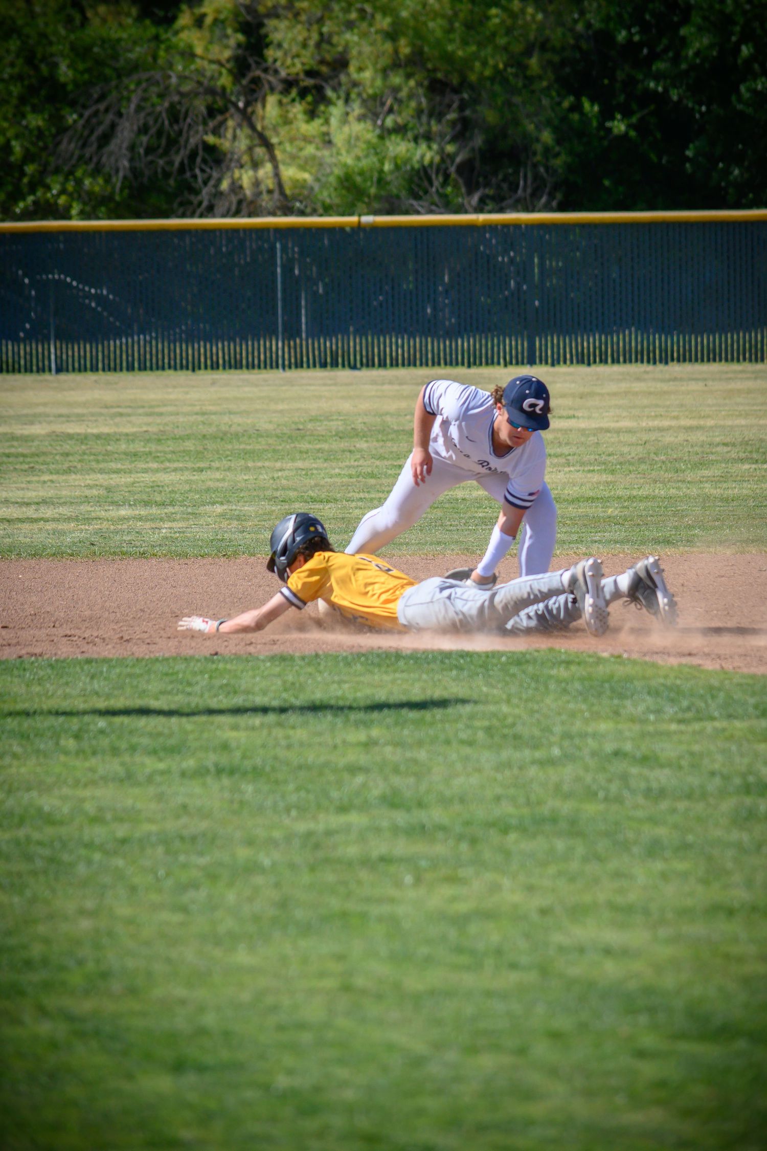 Baseball players collide during sliding play on the infield dirt.