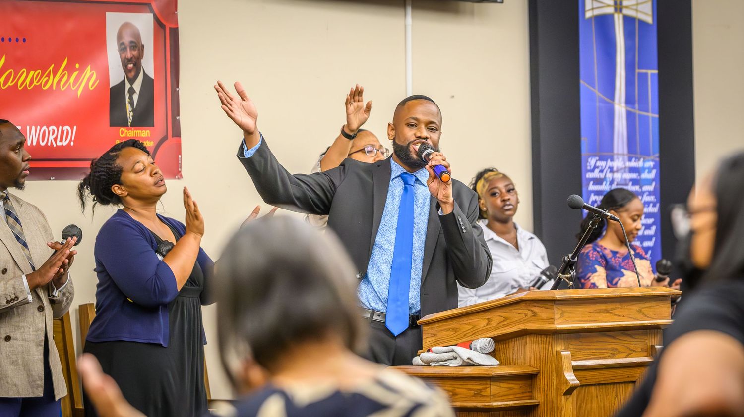 Congregation raises hands during worship service in church setting.