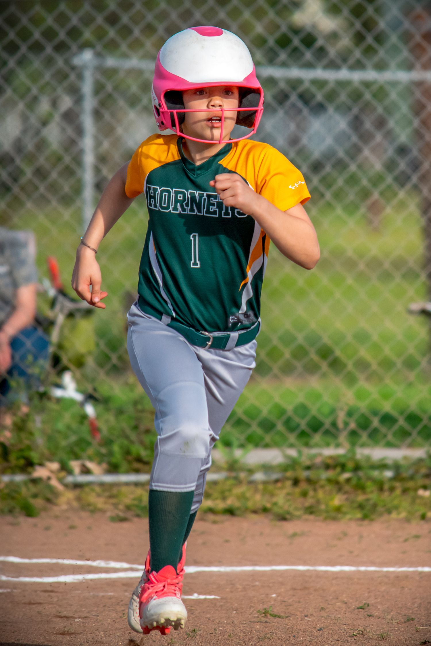 Young baseball player in green uniform running towards home plate during a game.