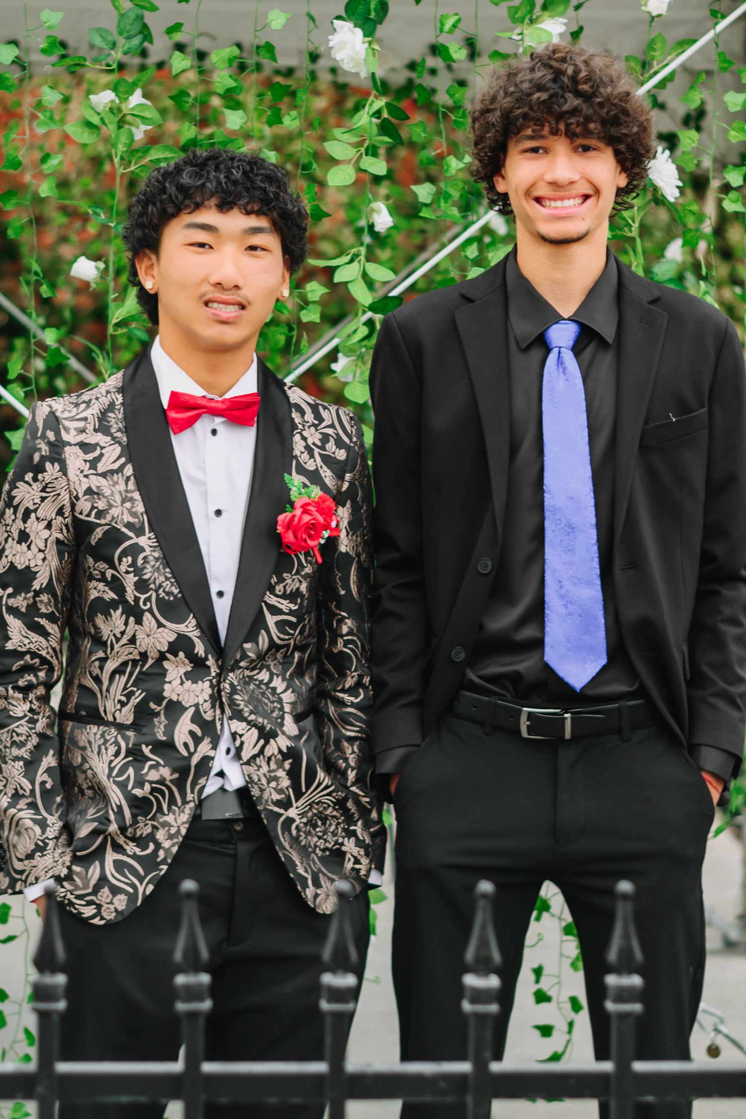 Two people in formal attire pose together against floral backdrop wearing matching ties.