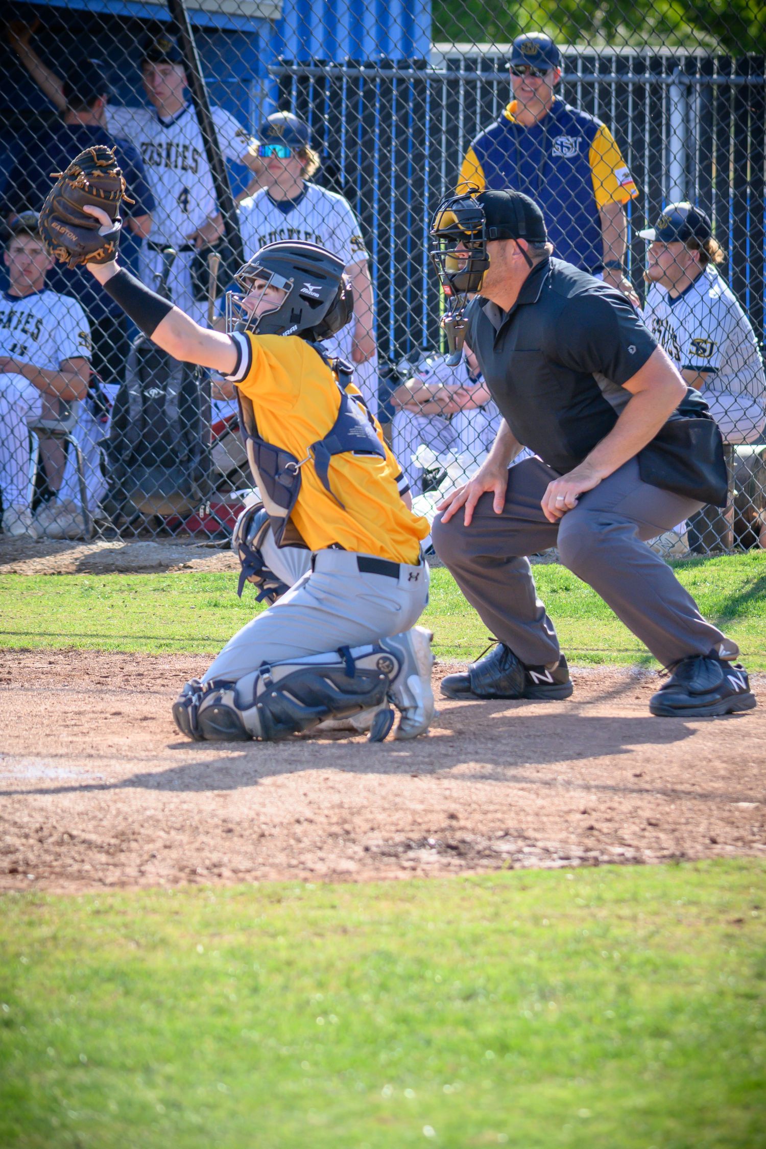 Baseball player in yellow uniform crouches at home plate while catcher prepares for the pitch during game action.