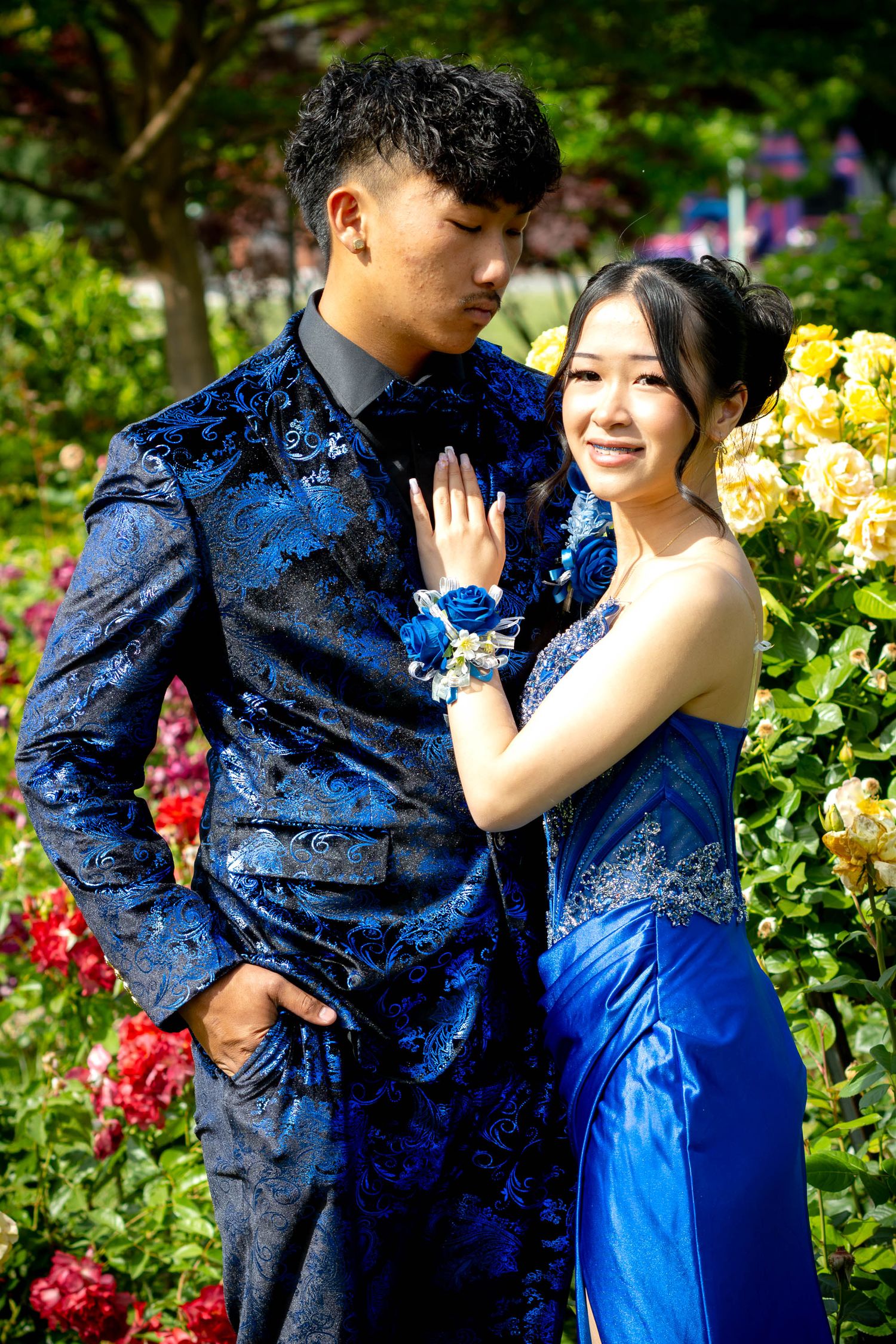 Couple in matching blue outfits posing in a colorful rose garden for prom photos.