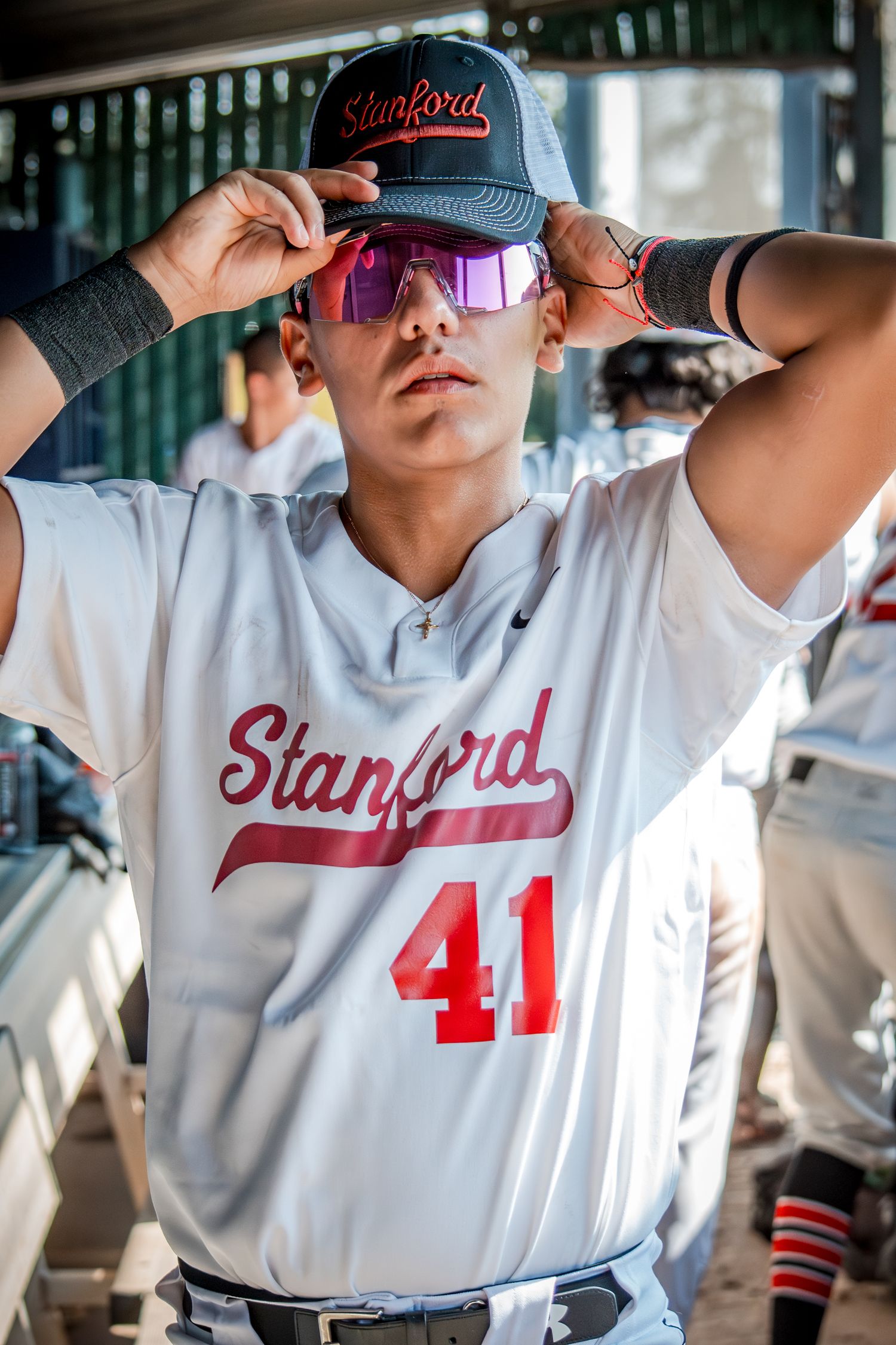 Baseball player wearing Stanford uniform number 41 adjusts cap and sunglasses in dugout.