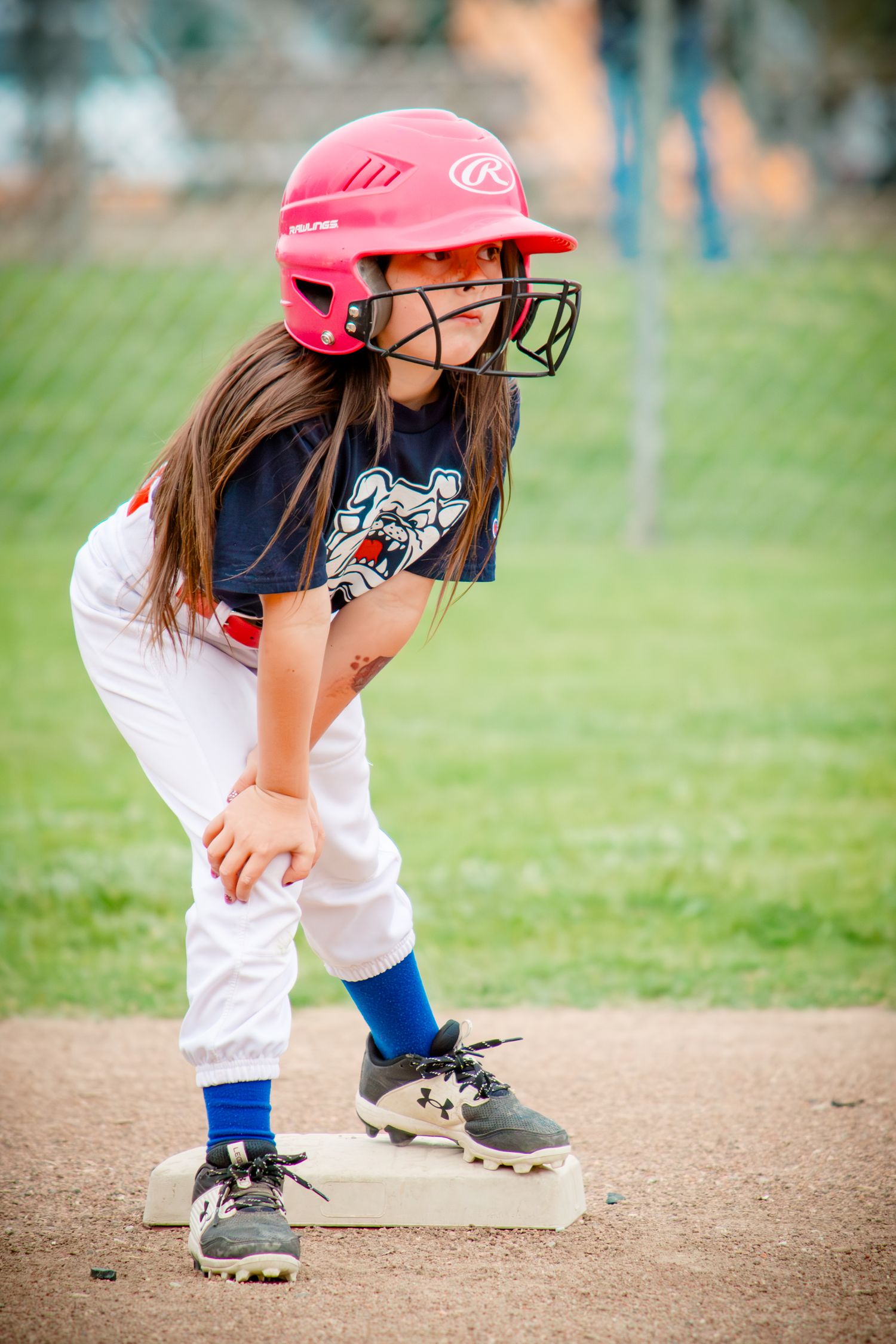Young softball player in pink helmet takes batting stance on baseball diamond.