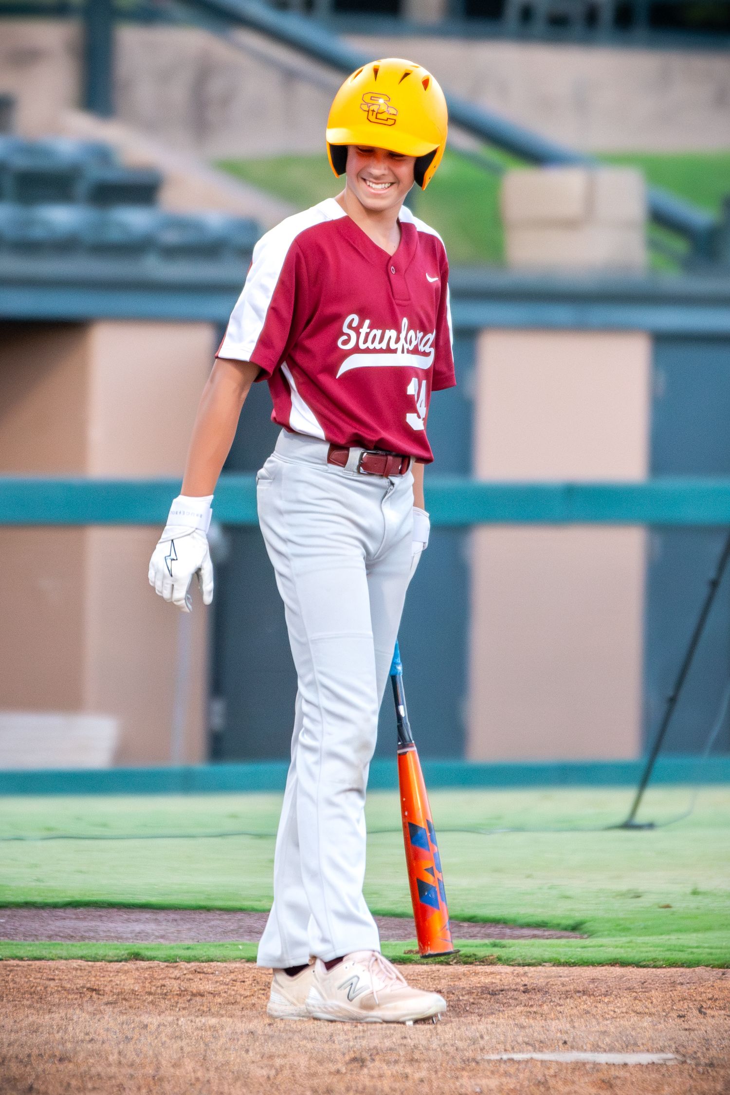 Baseball player wearing yellow helmet and maroon uniform stands ready at home plate during a game.