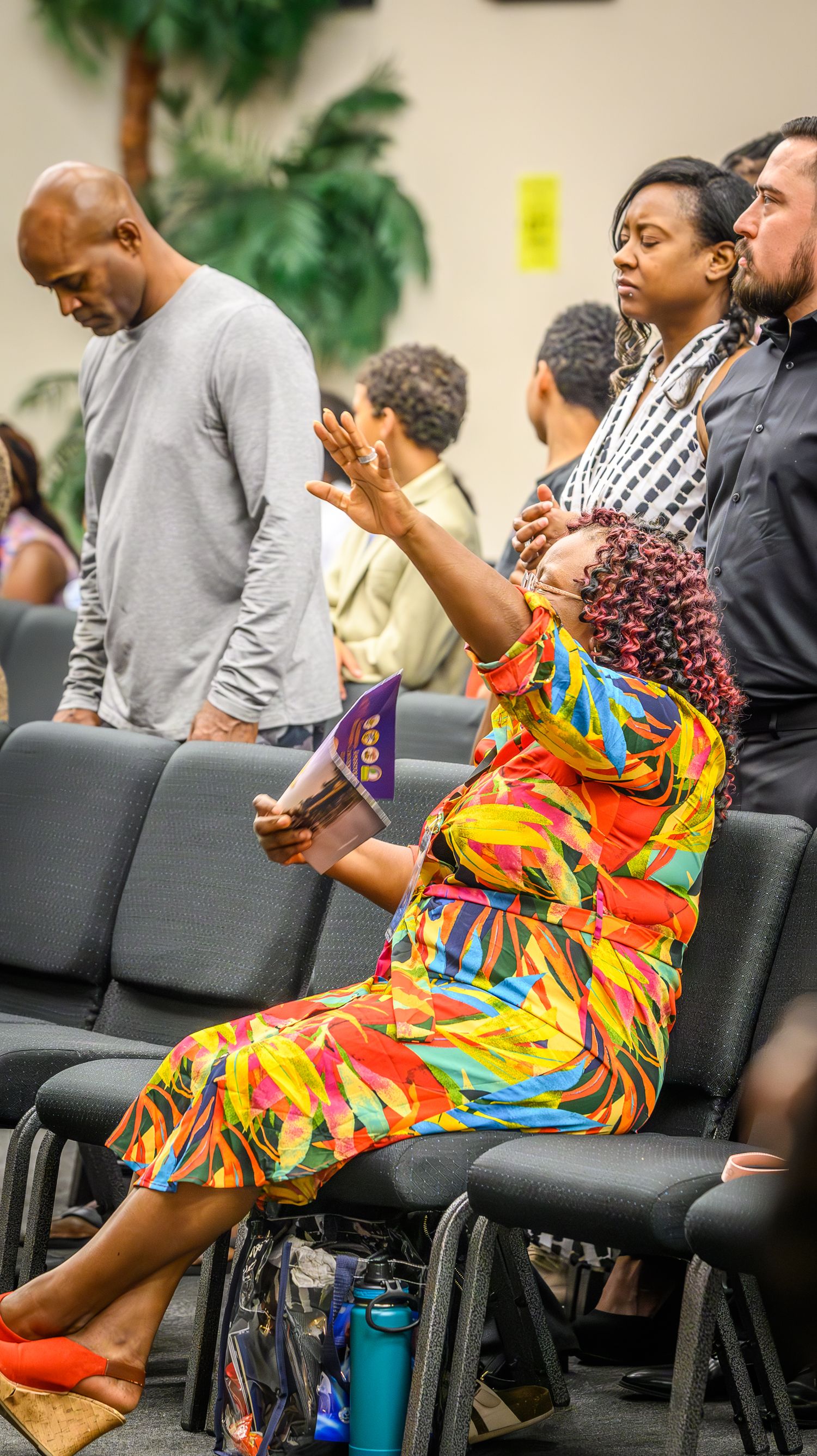 Worshippers in vibrant dress raise hands during church service.