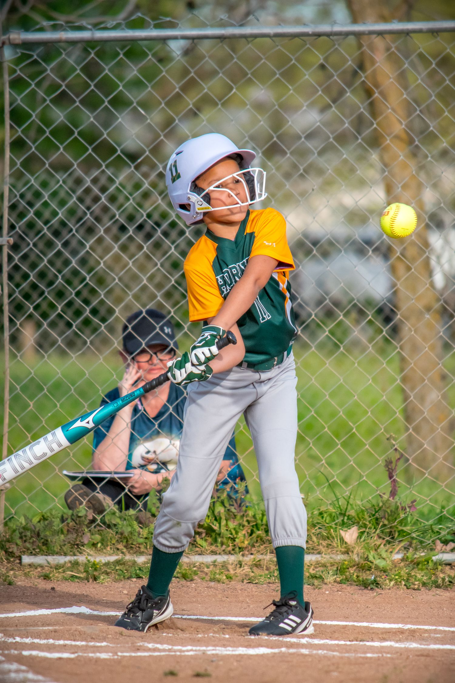 Sequence showing young softball batter in green uniform hitting a pitch on dirt field.