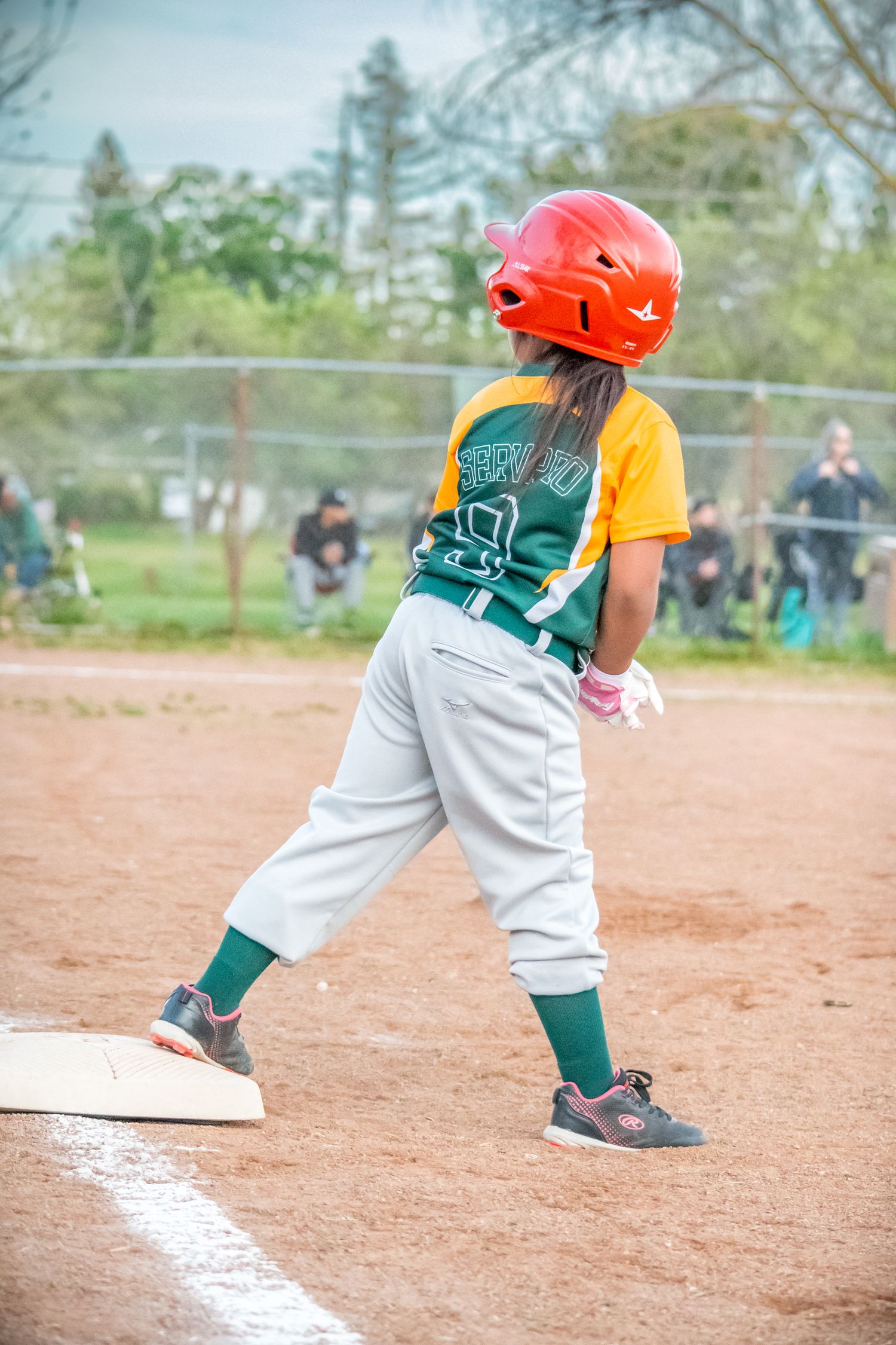 Youth Softball player in green uniform running along baseline during game.