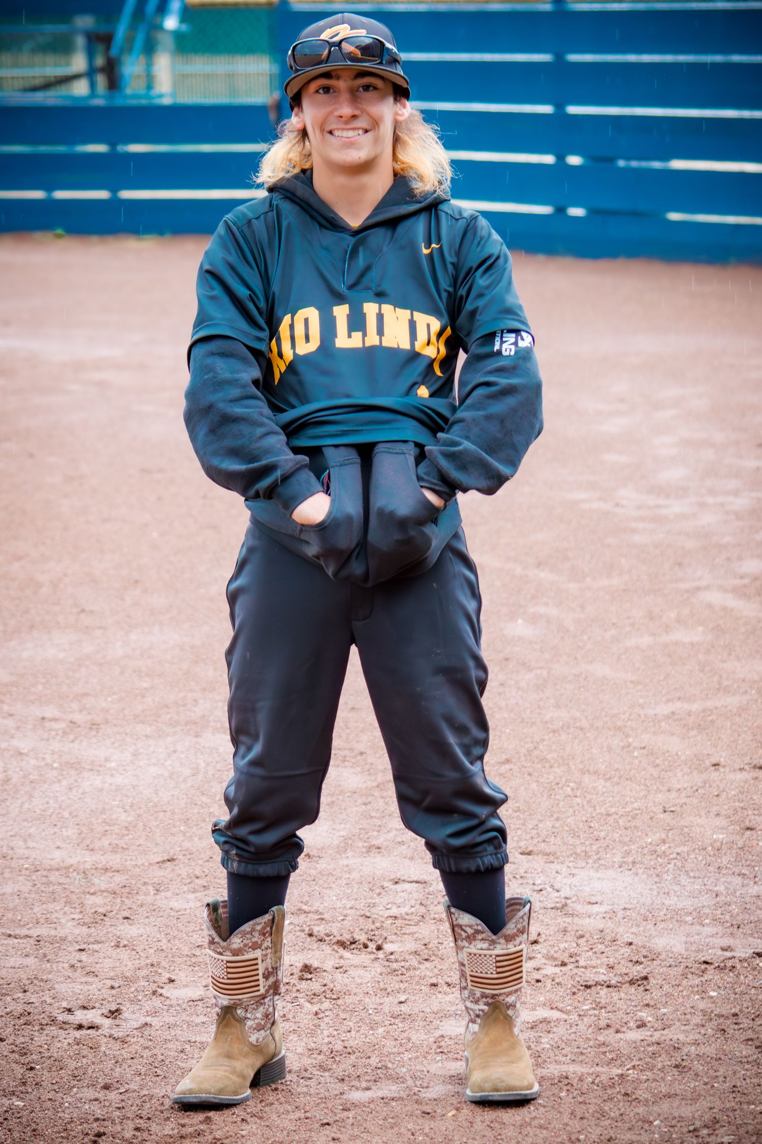 Young baseball player in navy uniform and tan boots stands on baseball field.