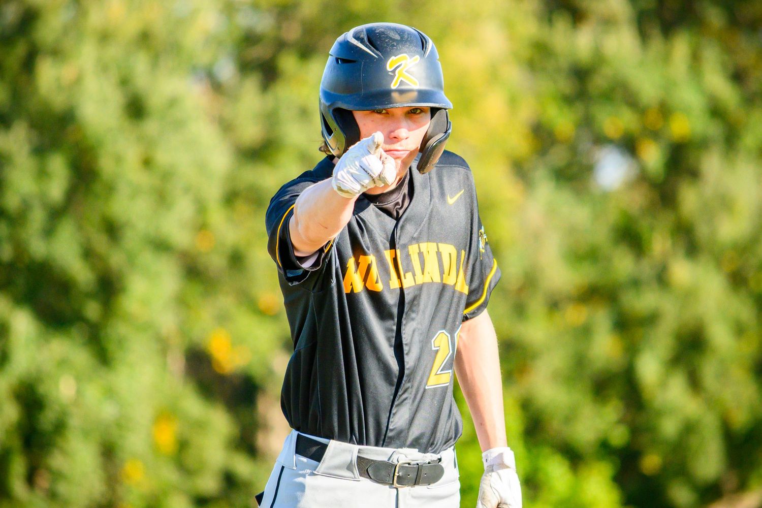 Baseball player in black and yellow uniform taking practice swings on sunny day.