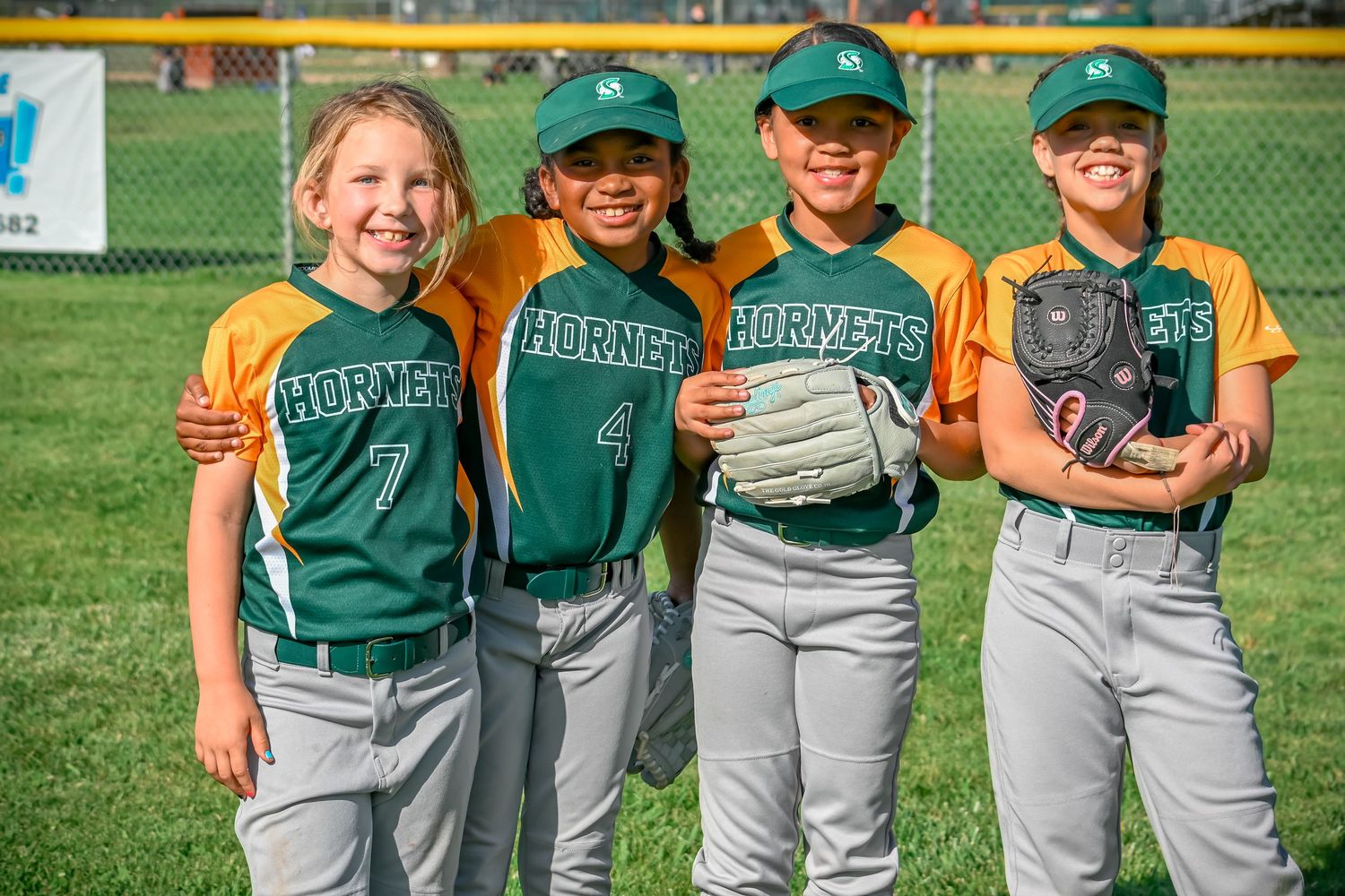 Youth Softball team lined up in green and yellow uniforms on field.