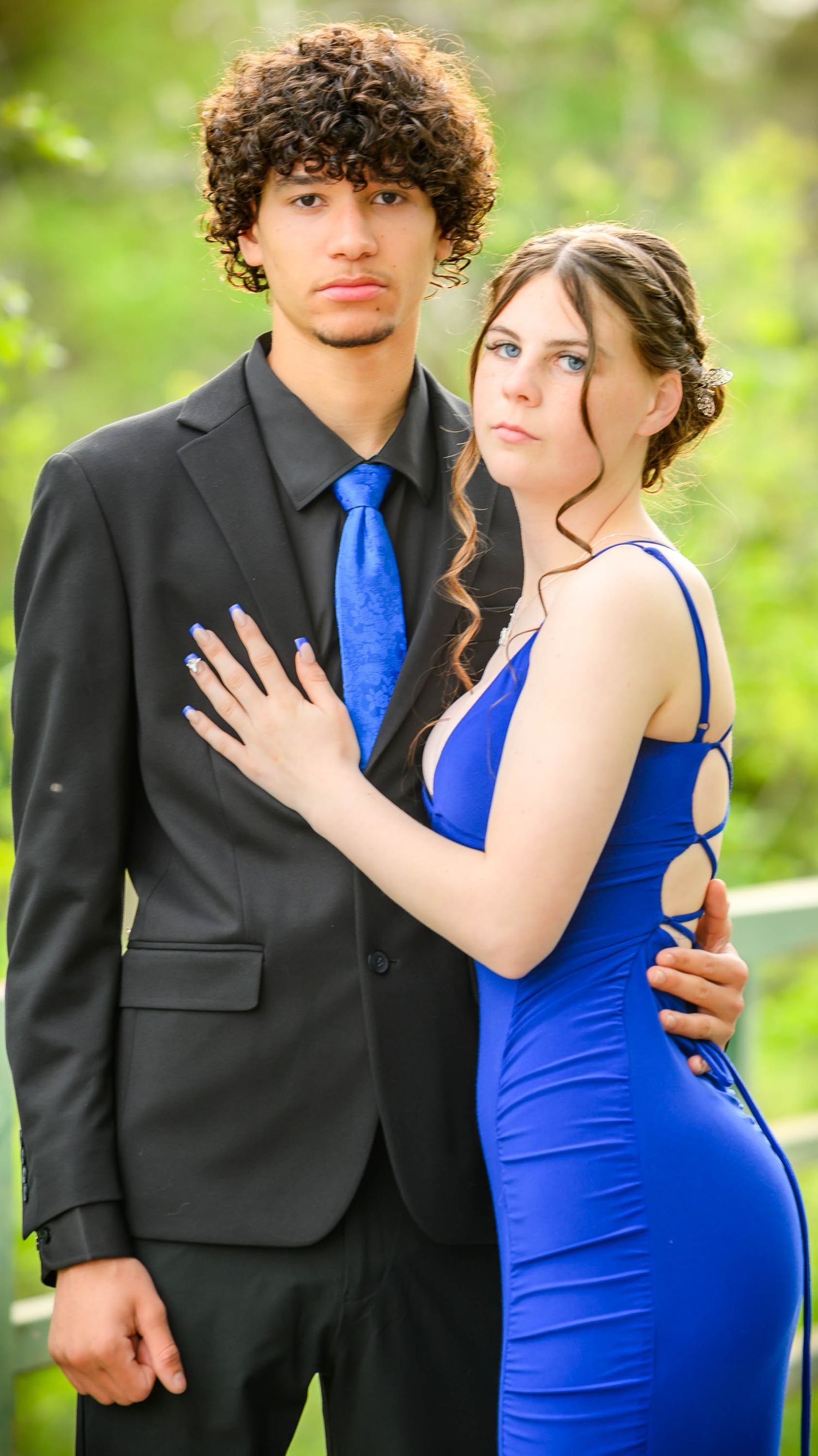 Couple in formal wear with blue tie and dress posing outdoors.