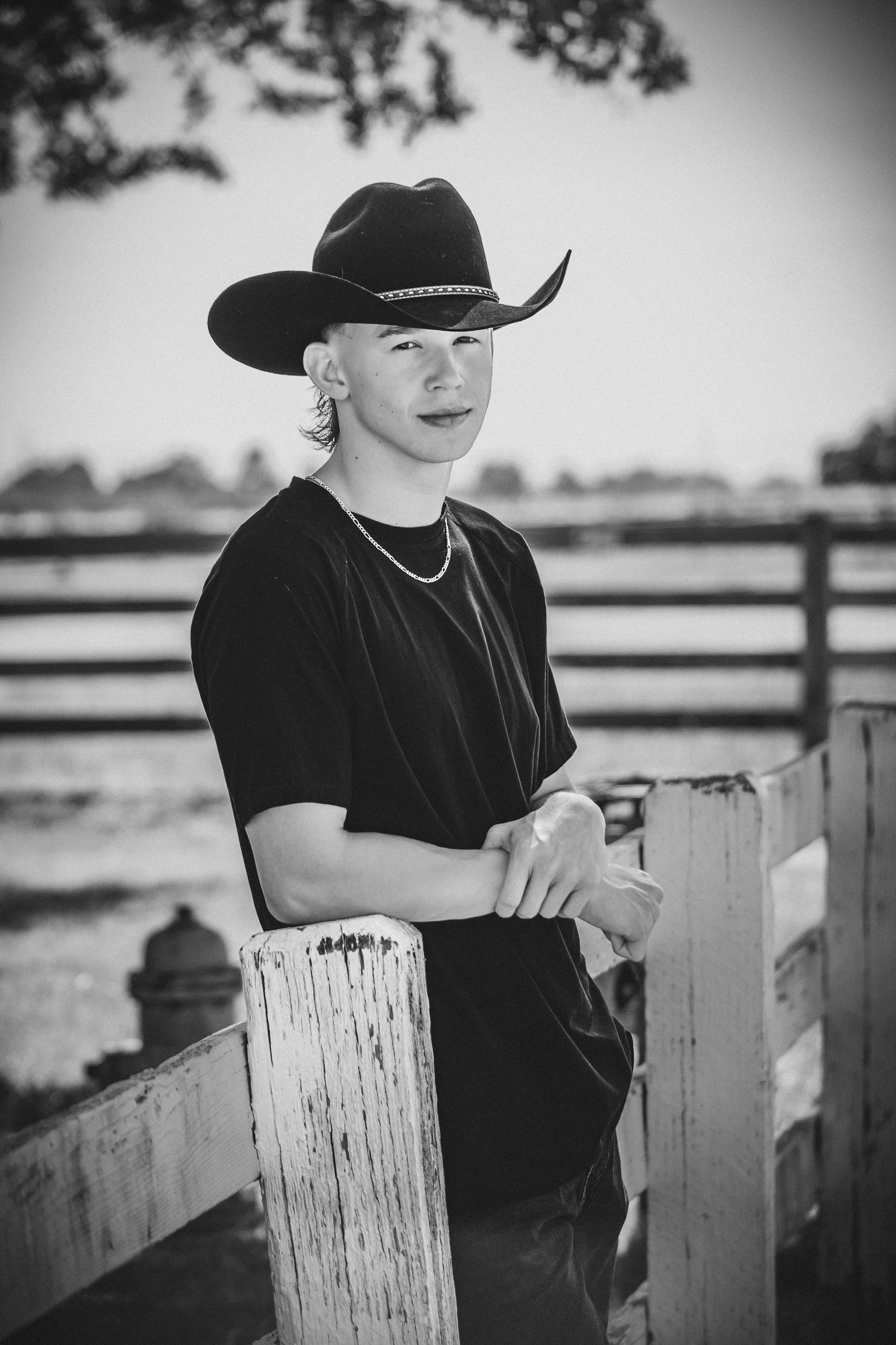 Black and white portrait series leaning on wooden fence post wearing western attire.
