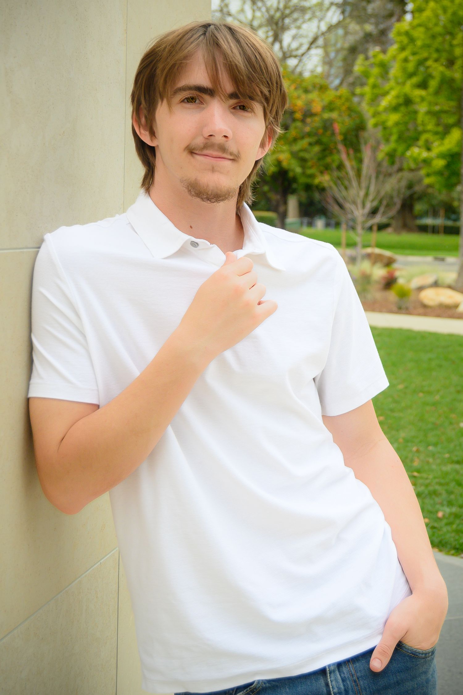 Outdoor portrait against cream wall in white polo shirt.
