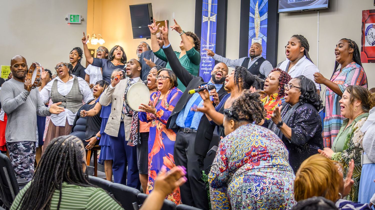 Congregation members worshipping with raised hands in a church sanctuary with decorative banners.