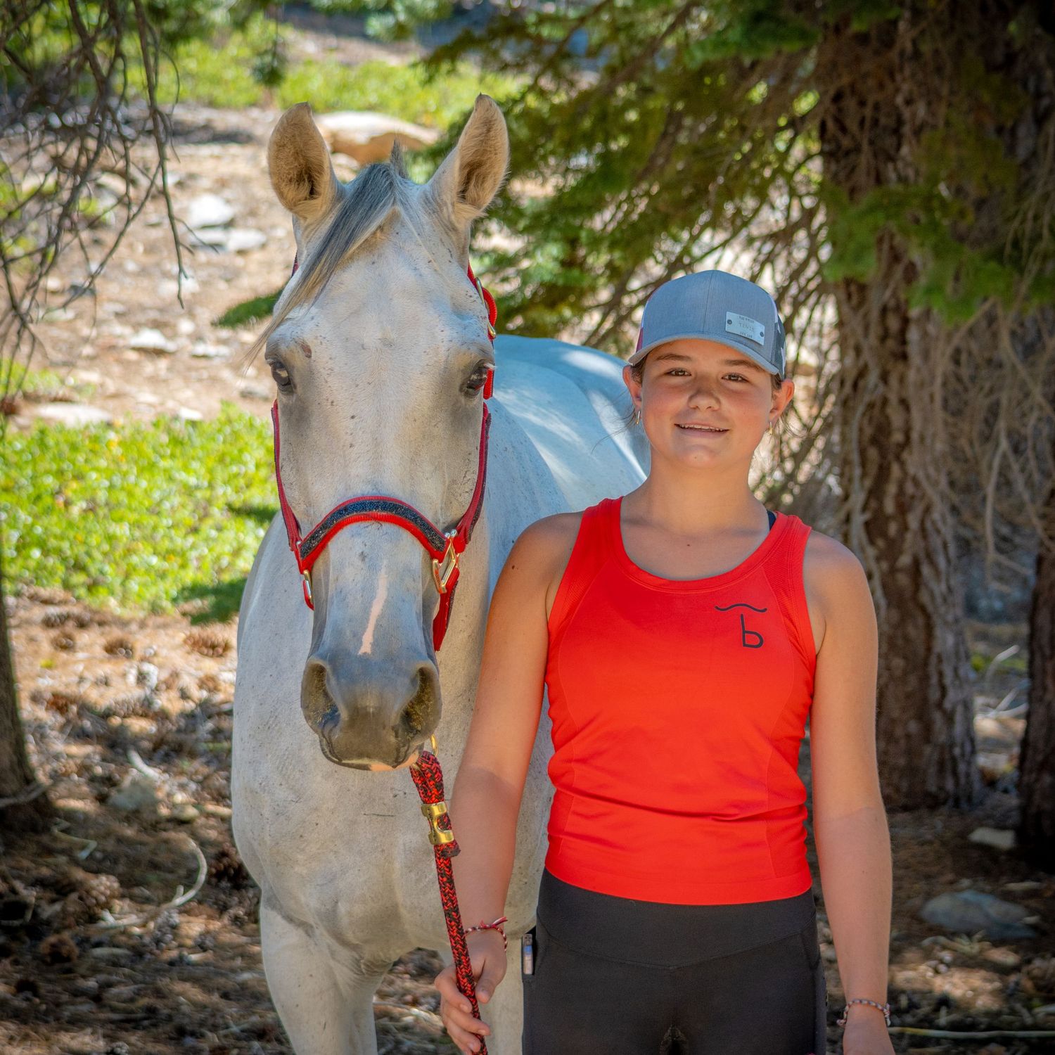 A horse poses with someone wearing a bright red tank top in a sunny outdoor setting.