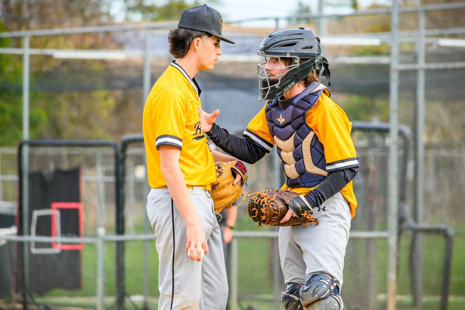 Youth baseball players in yellow uniforms communicate during a game on a sunny day.