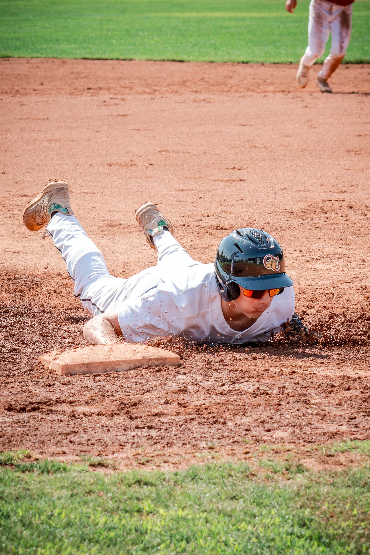 A baseball player wearing white uniform slides into base during intense game action.