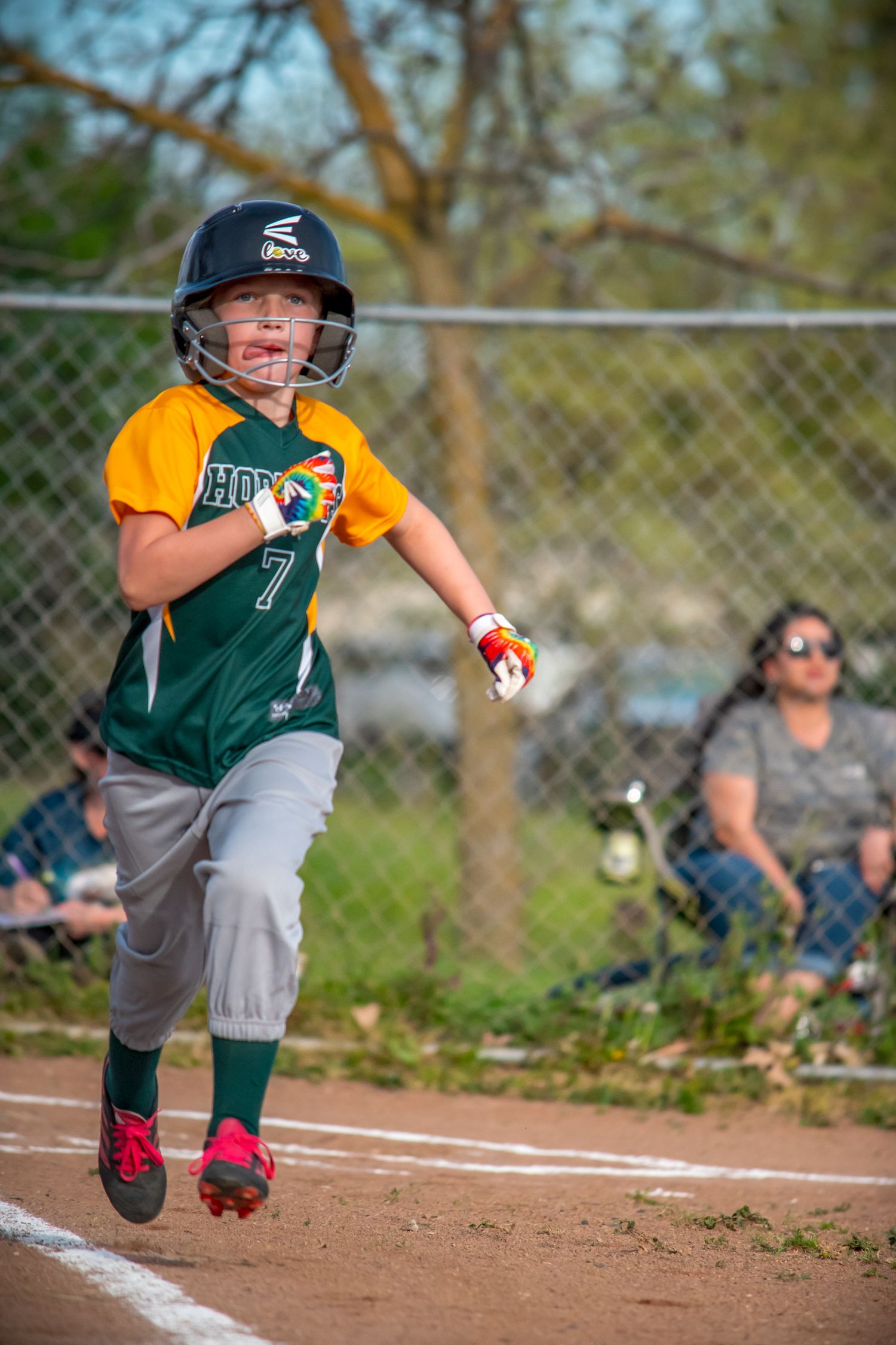 Softball player in green and yellow uniform sliding into base during a youth sports game.