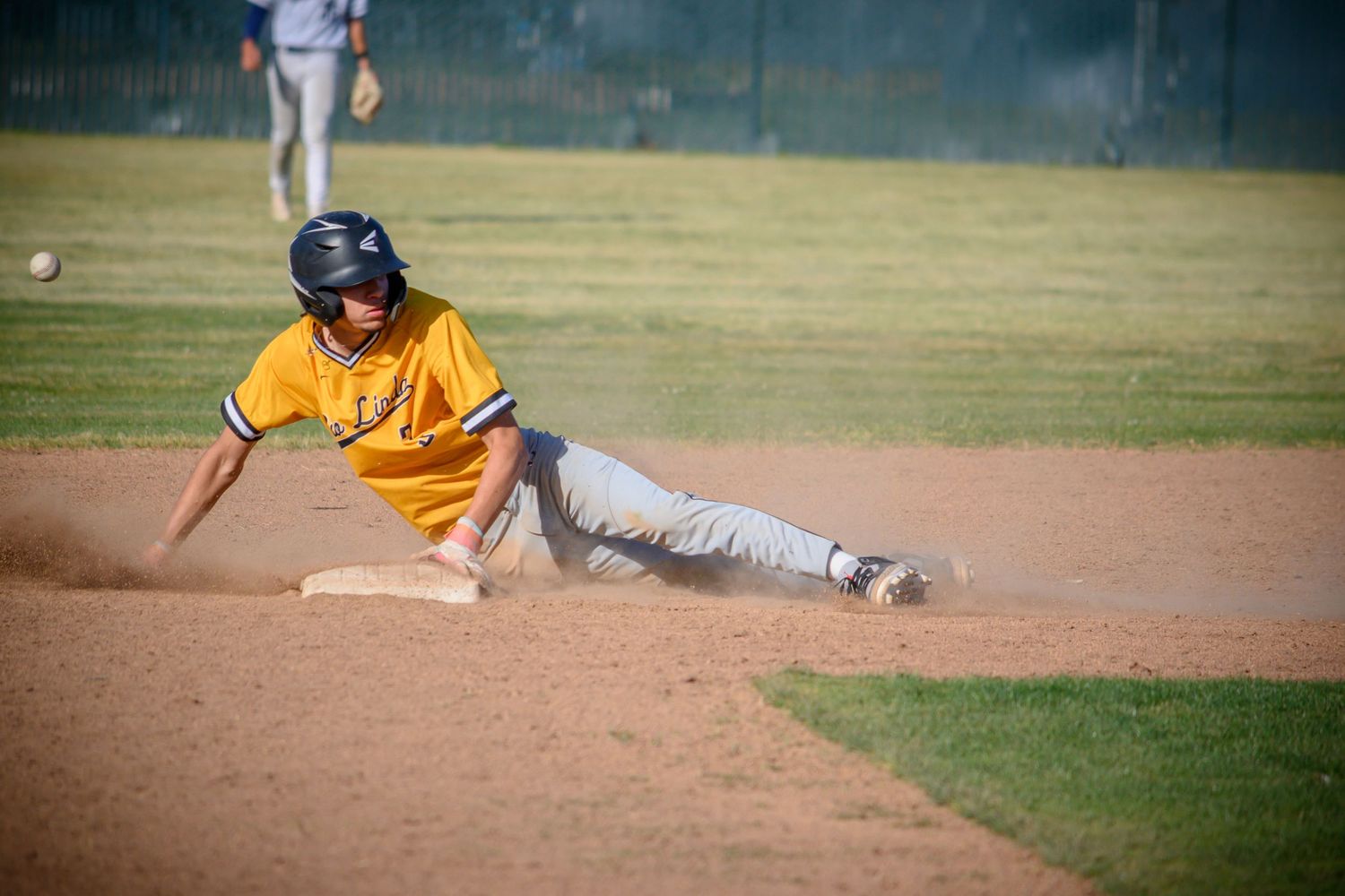 Baseball player in yellow uniform slides on dirt infield during game.