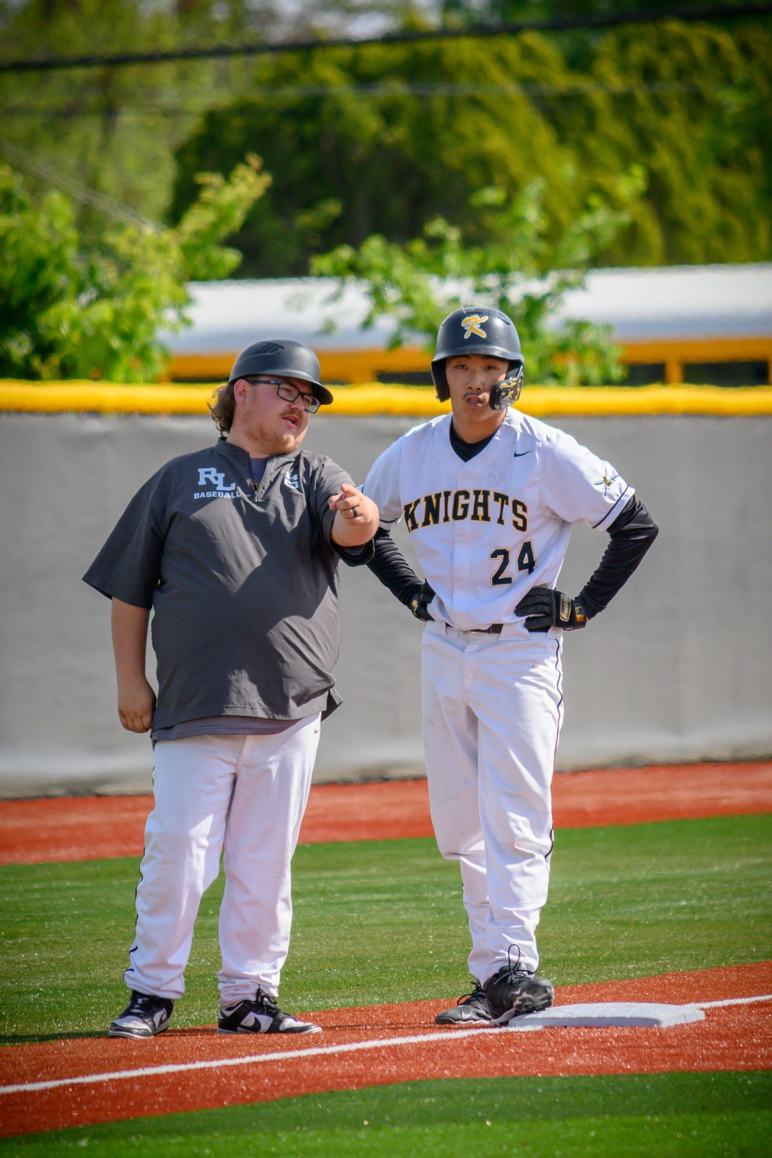 Baseball coach and player stand together on the field while having a discussion during practice.