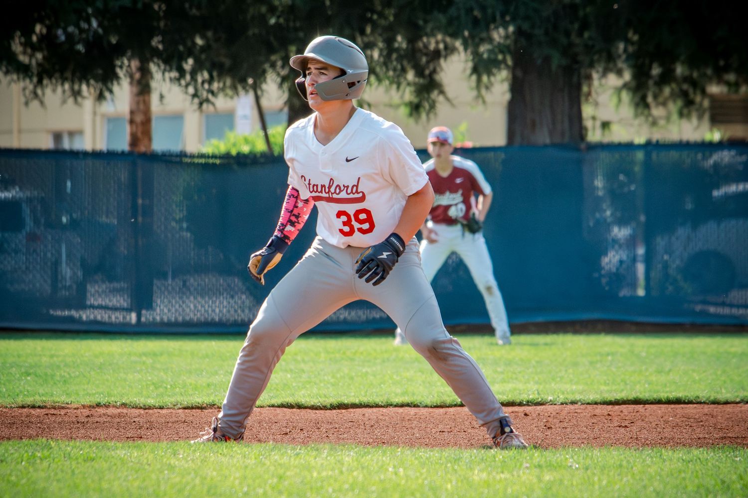 Baseball player in white uniform and blue cap throws pitch from mound during game on sunny day.